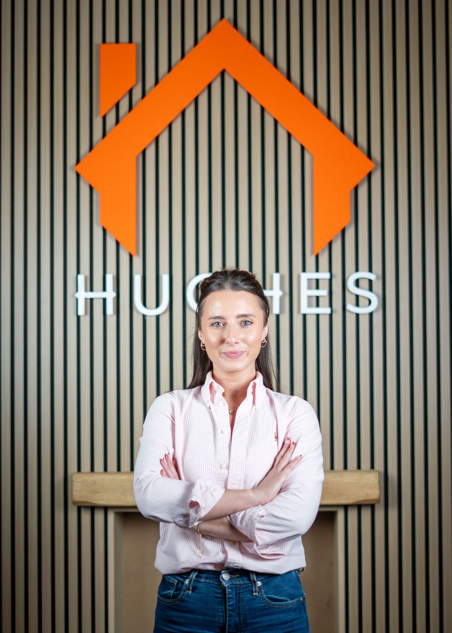 Business professional in white shirt stands confidently against wood paneled wall with orange accents.