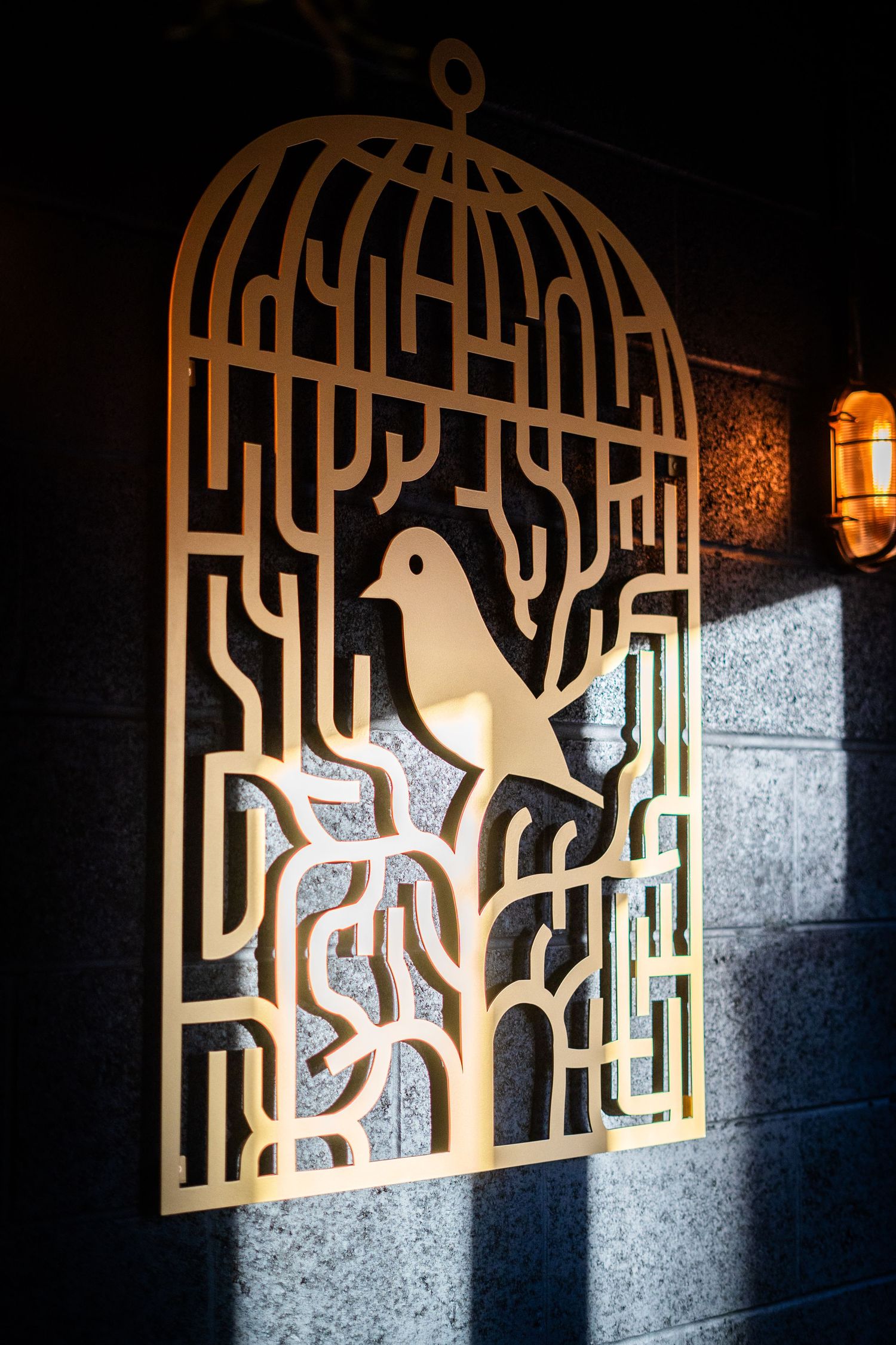 Decorative gold metal wall art featuring a bird in an intricate cage design with geometric patterns.