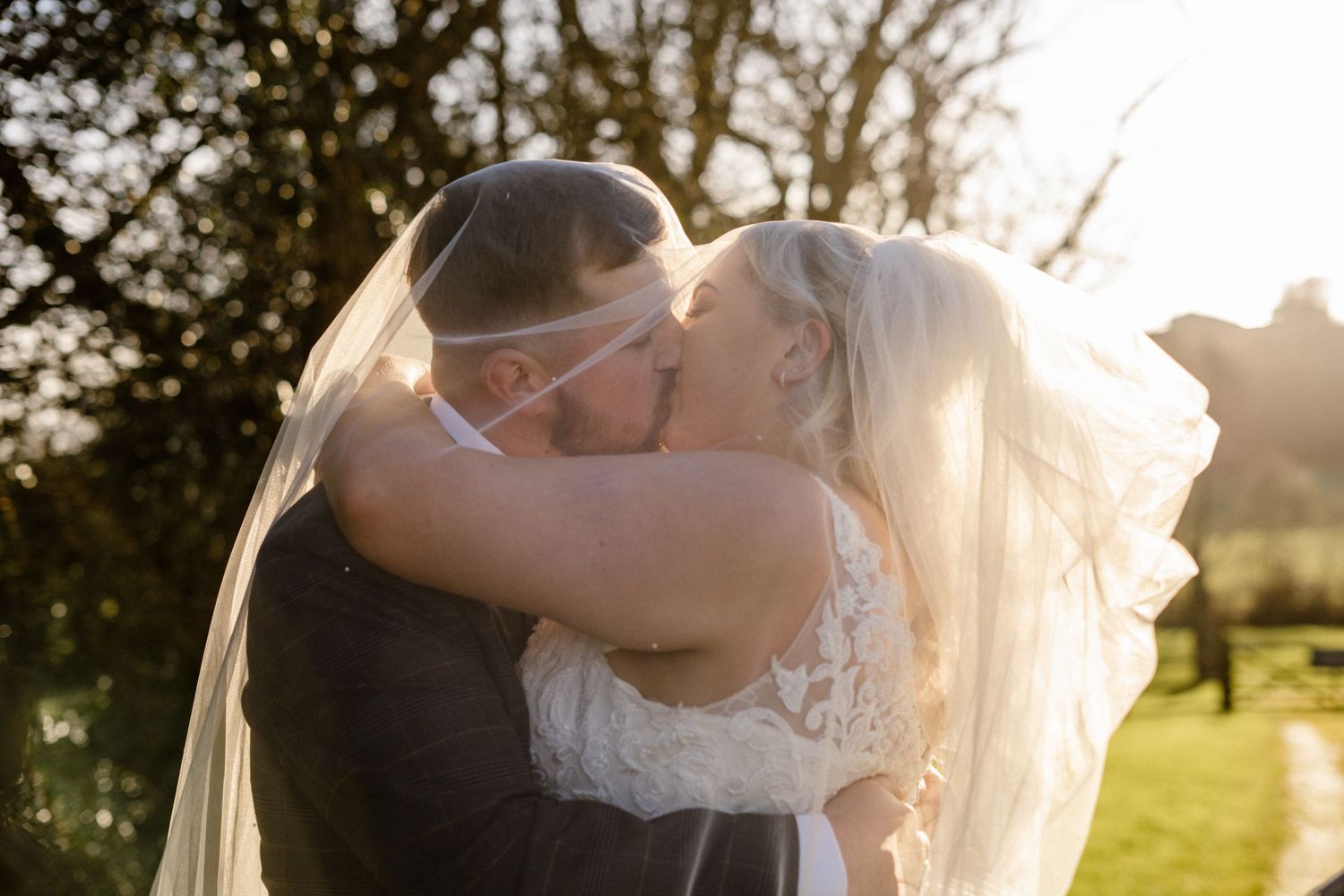 Romantic sunset wedding portrait with golden light filtering through trees.