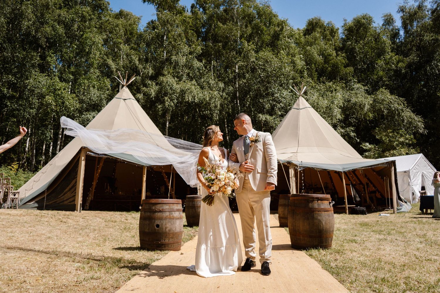 Rustic outdoor wedding setup with white canvas tents and wooden barrels in a natural setting.
