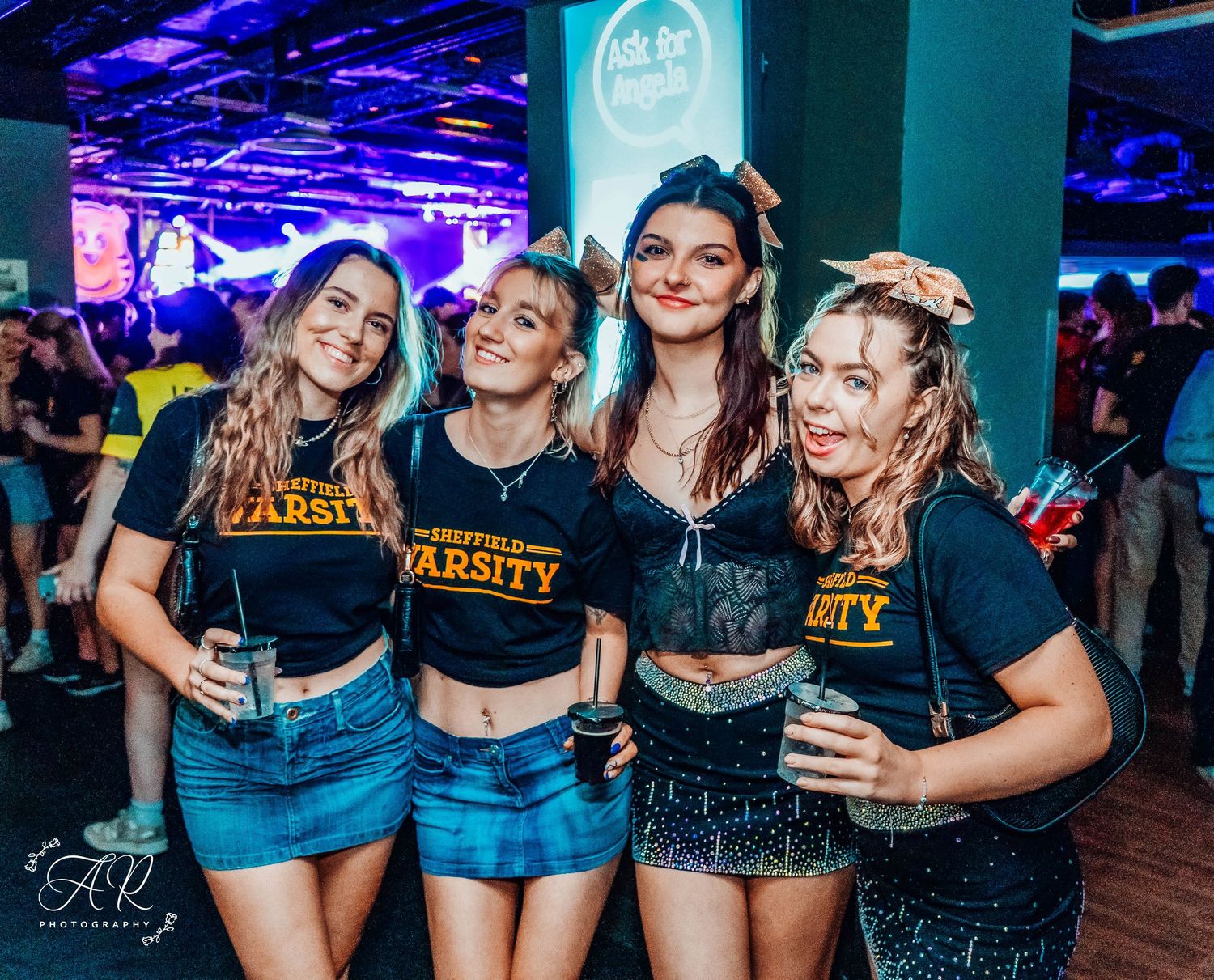 Friends wearing matching black shirts and denim shorts pose together at a nightclub event.