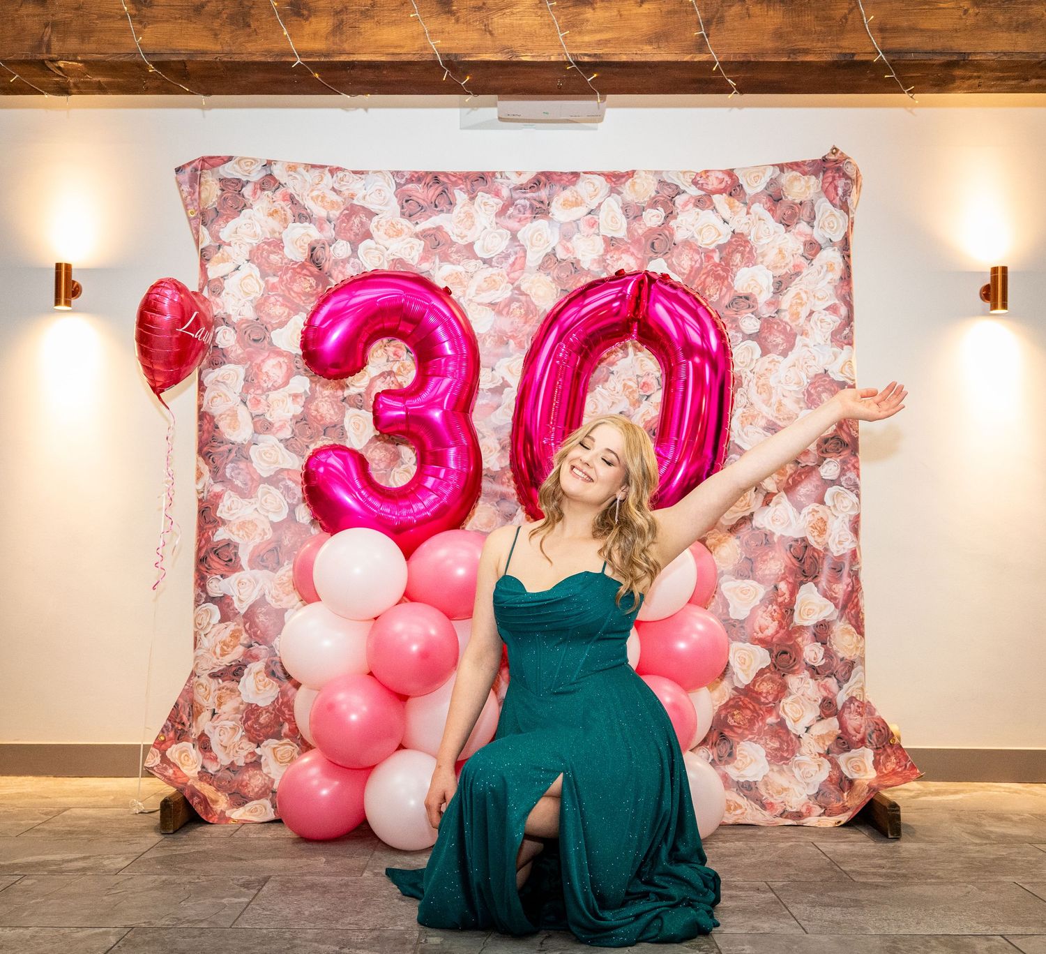 Elegant teal gown photographed against a pink floral backdrop with balloon decorations.