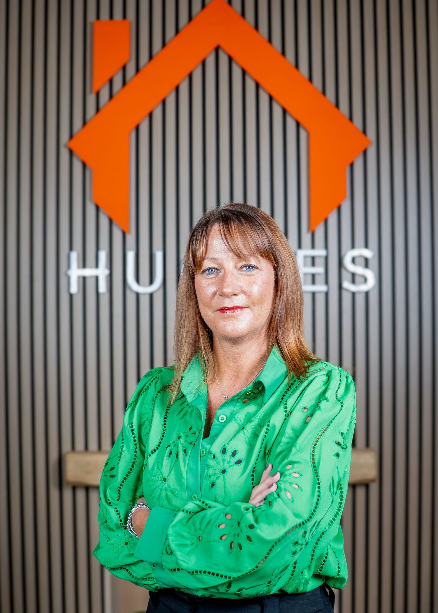Woman in emerald green top stands confidently against modern office backdrop.