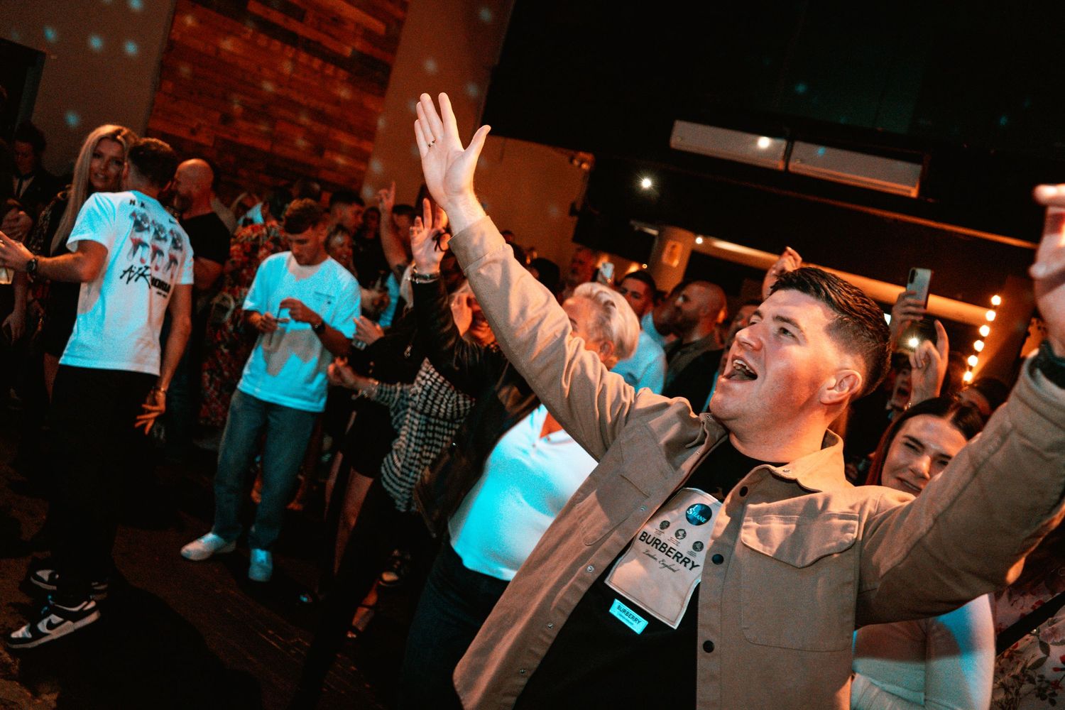 Energetic performance scene with audience members raising hands in a dimly lit venue.
