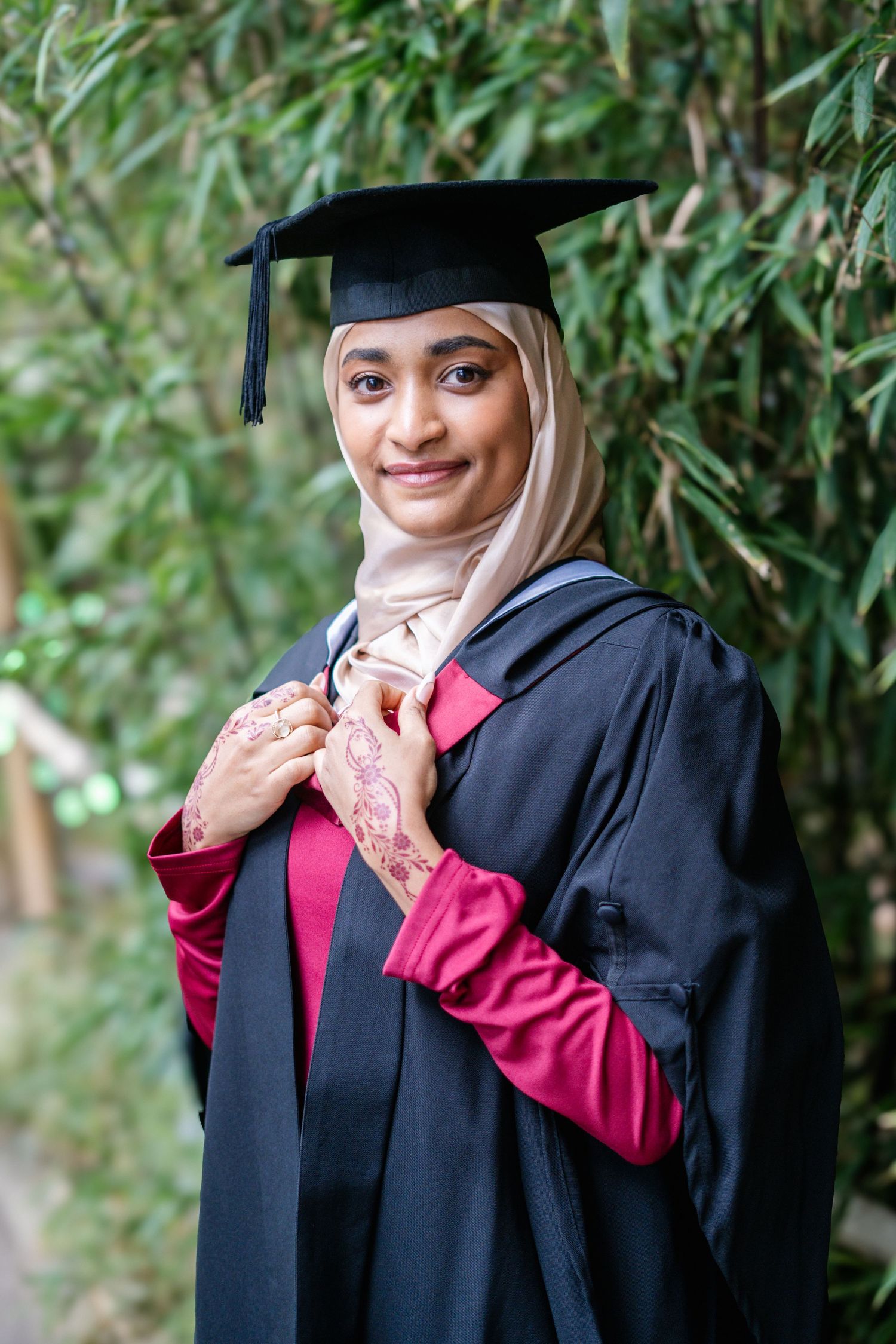 Graduate in traditional academic regalia poses among garden greenery.