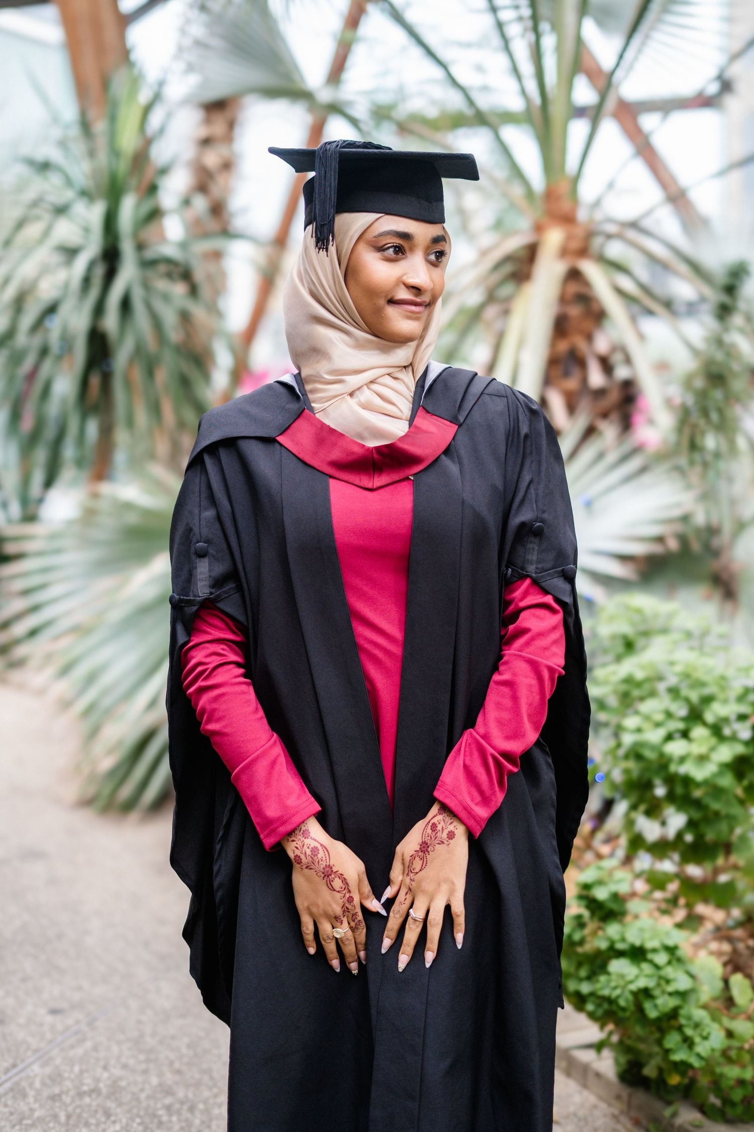 Graduate displays decorated hands while wearing academic regalia in botanical setting.