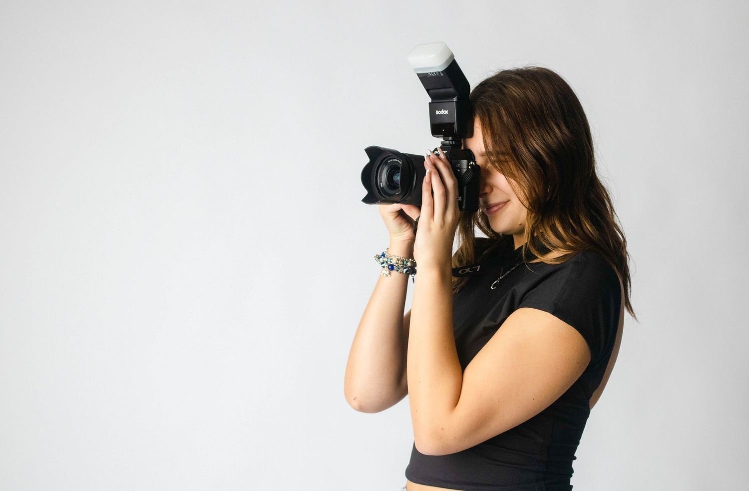 A photographer taking pictures with a professional DSLR camera against a white backdrop.