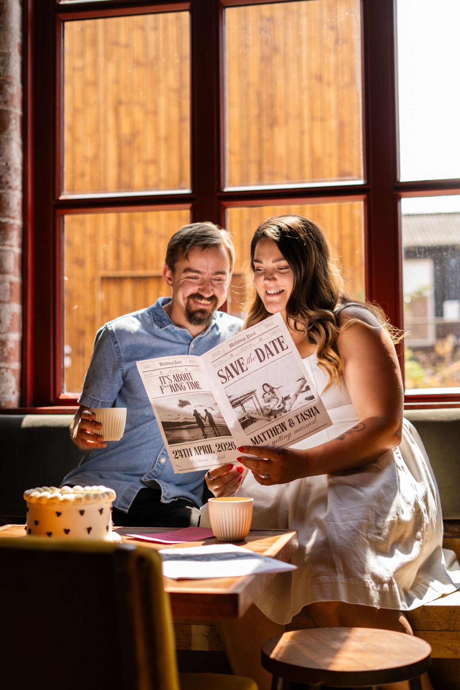 A couple reads a save-the-date announcement together in a sunlit room.