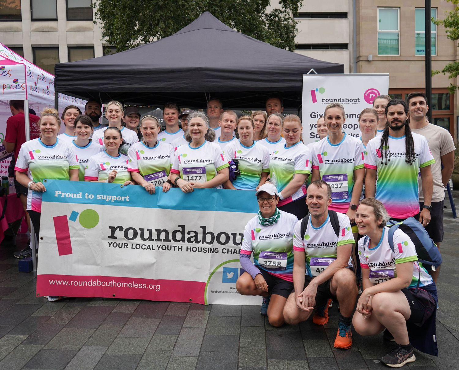 Group of runners in matching t-shirts pose with Roundabout charity banners at an outdoor event.