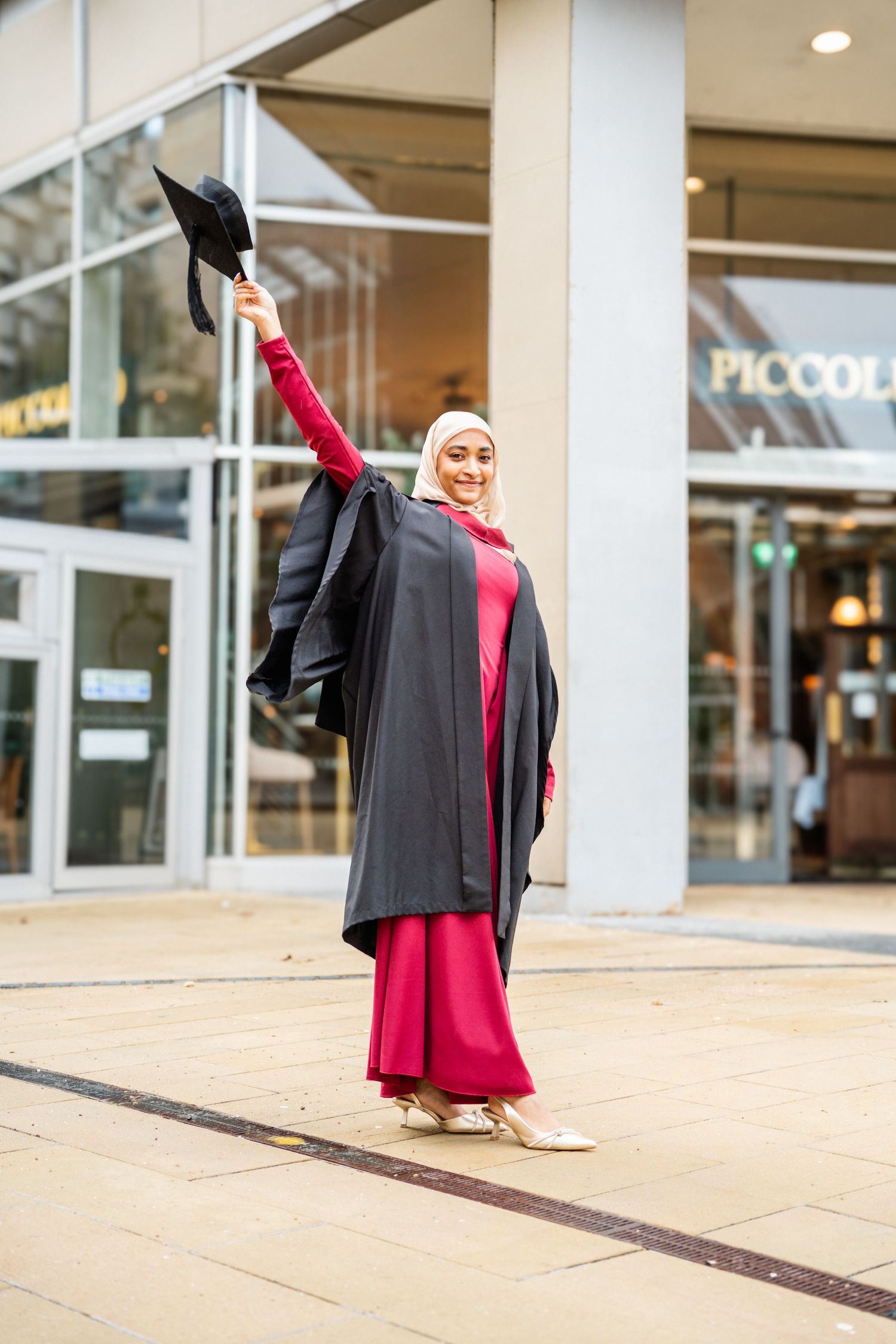 Graduate in black and red academic regalia celebrates achievement with joyful poses.