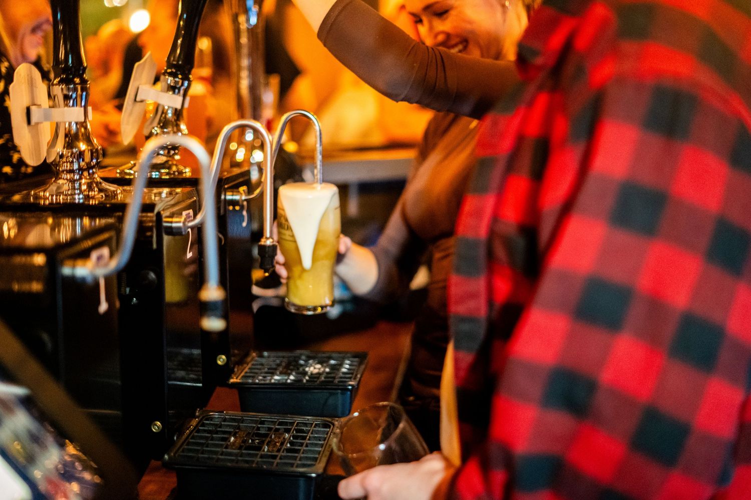 Close-up of beer being poured from tap with person wearing red plaid flannel shirt visible.