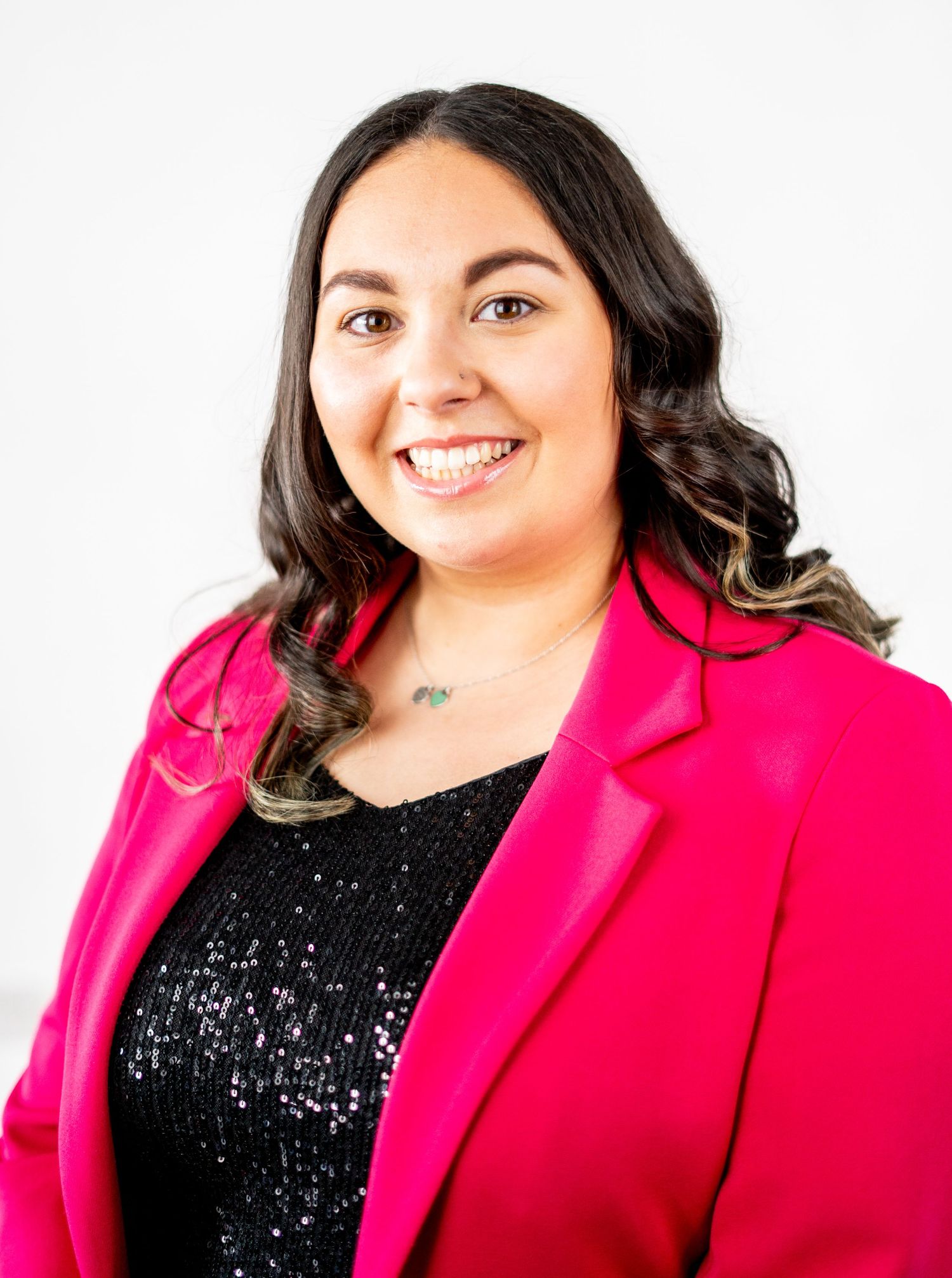 Professional portrait of a person wearing a bright pink blazer and sparkly black top.