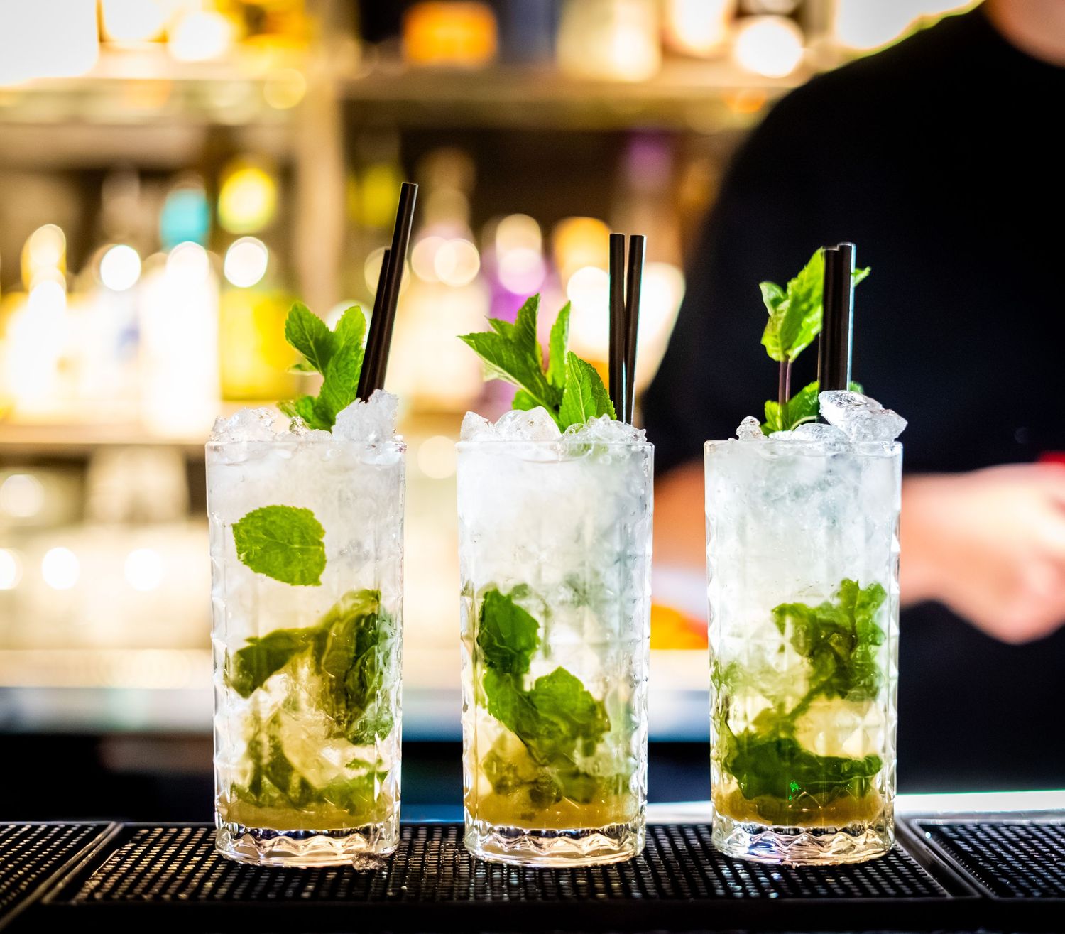 Three mojito cocktails with fresh mint leaves and crushed ice on a bar counter.