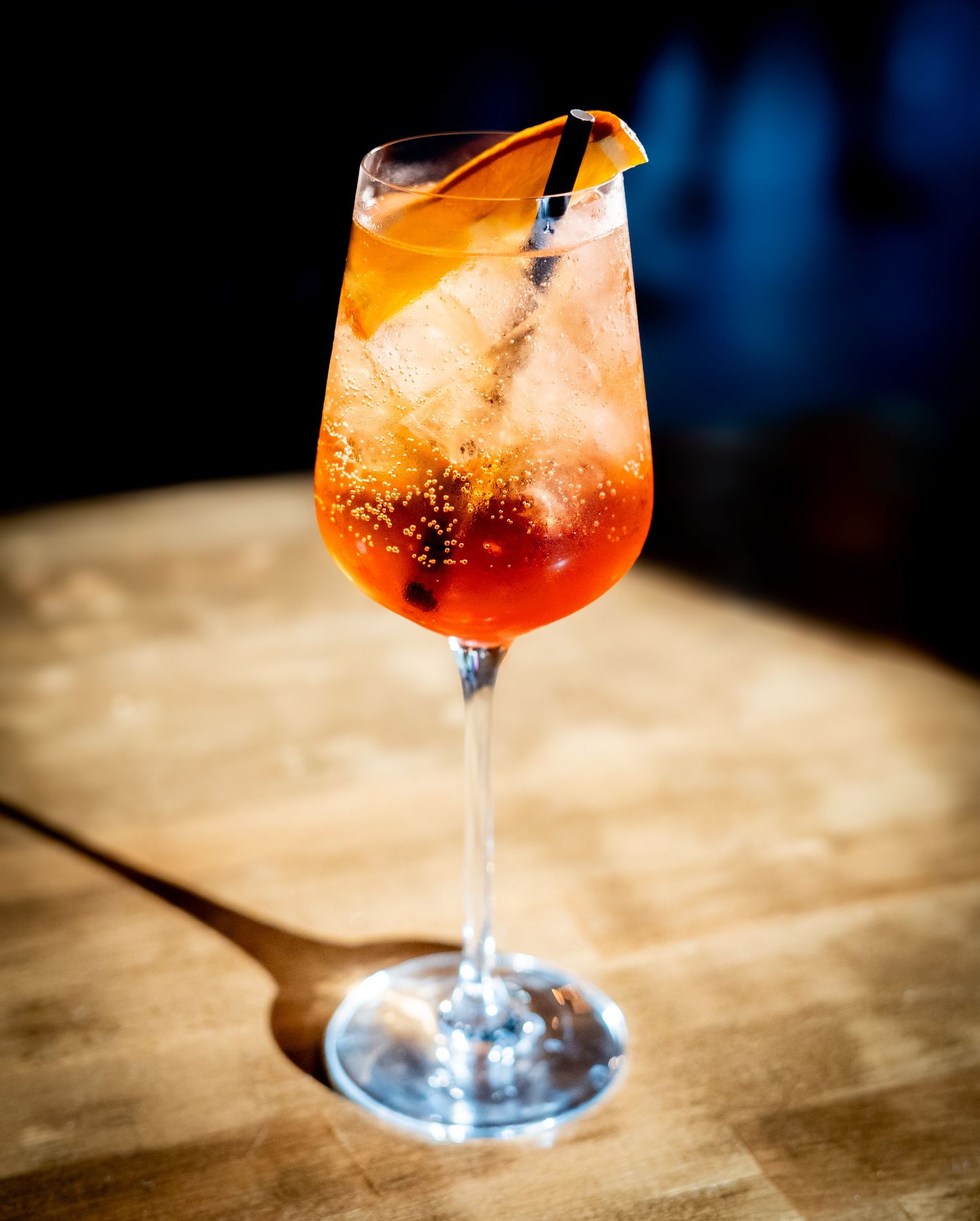 Aperol spritz cocktail with orange slice garnish on wooden bar surface.