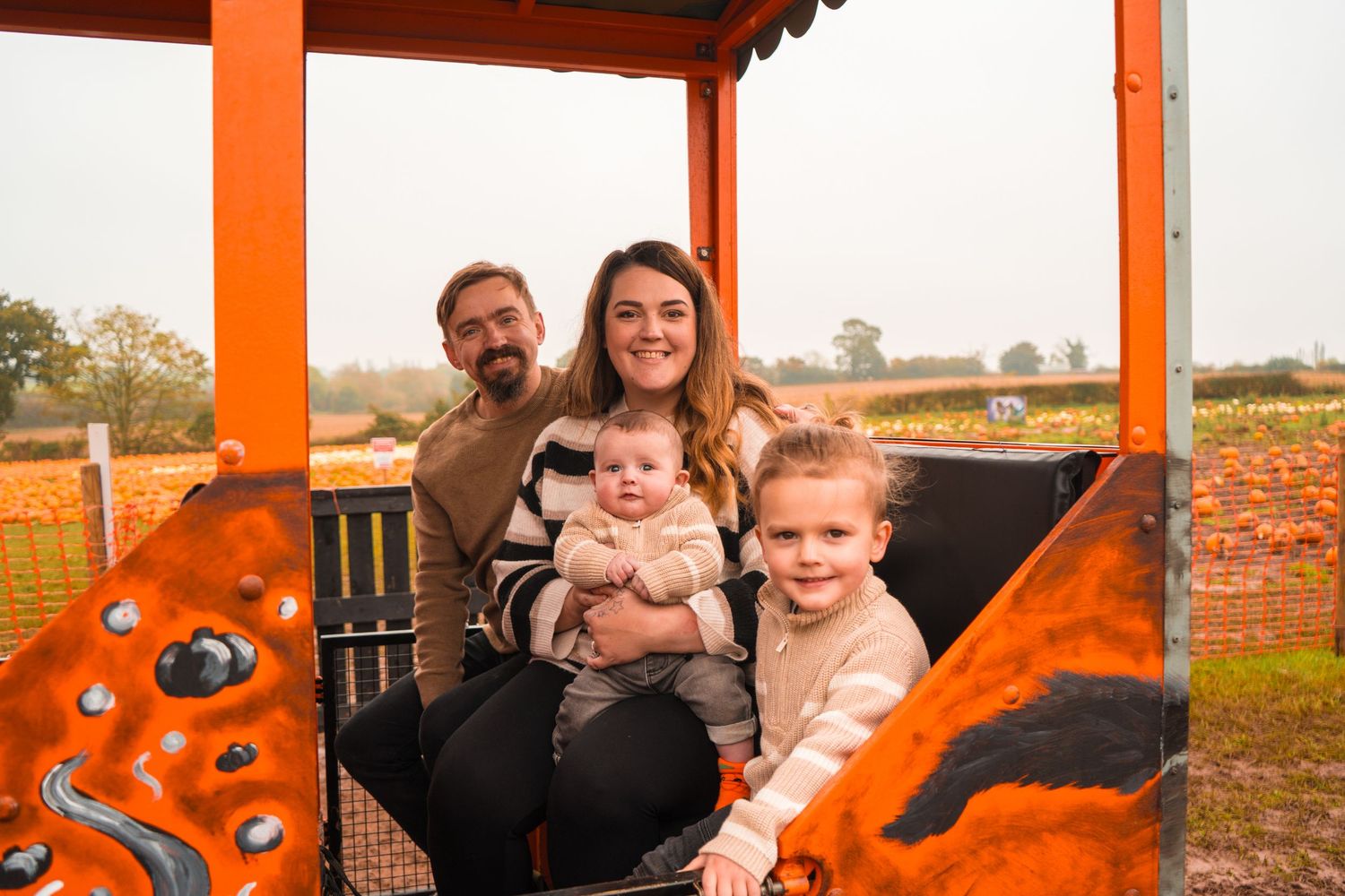 Family photo session under an orange-framed structure at a pumpkin farm.