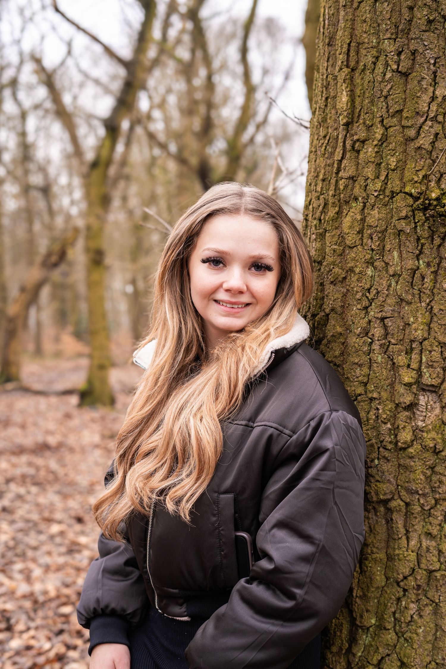 Portrait session against a large tree trunk in a forest setting.
