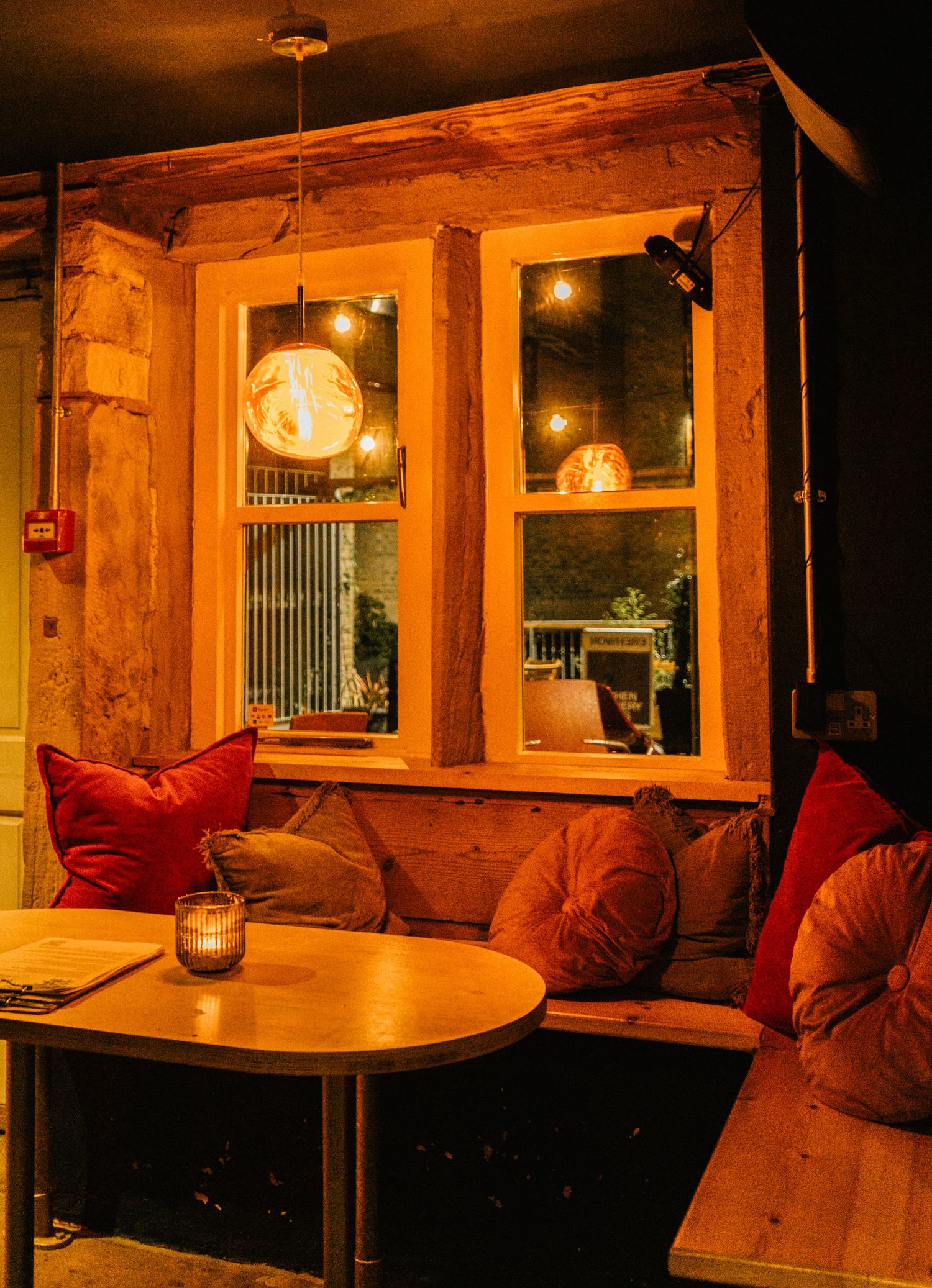 Cozy restaurant interior with warm lighting, wooden beams, and comfortable red cushioned seating along the walls.