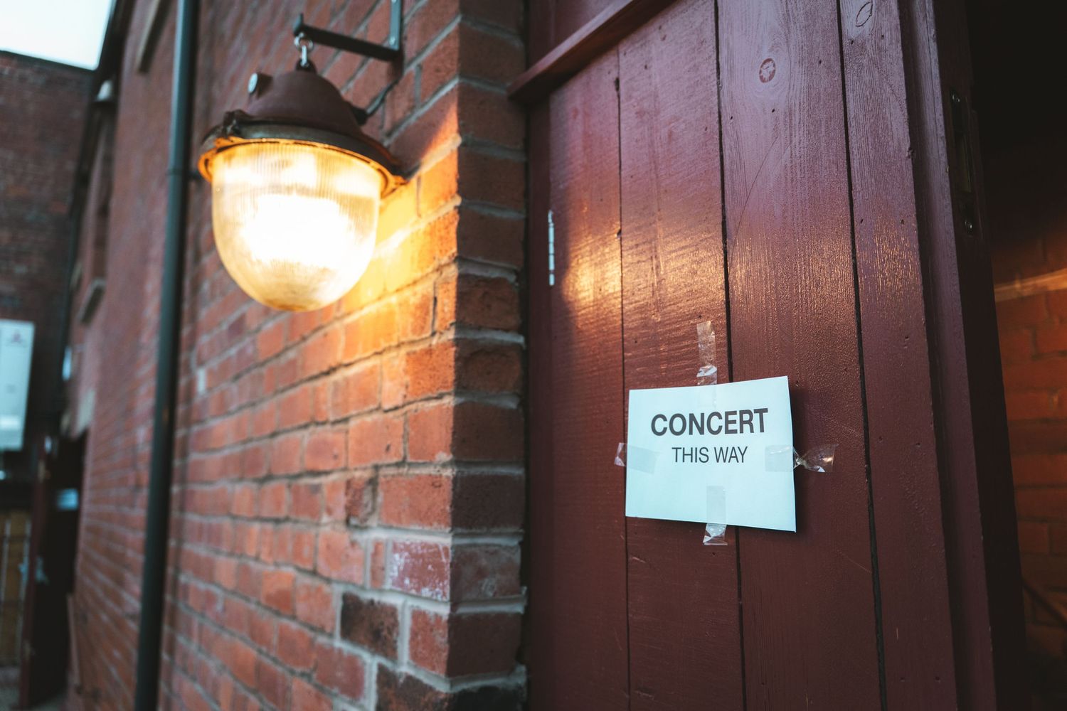 Brick wall with directional concert signs and warm lighting in a venue hallway.