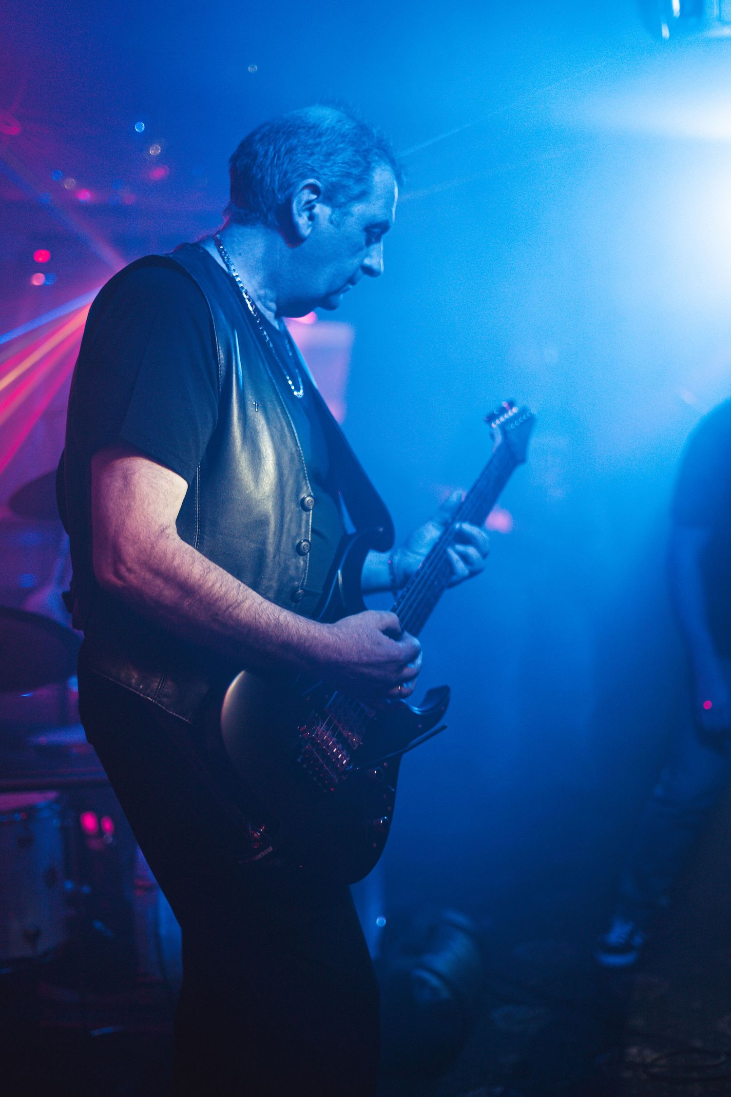 Guitarist playing electric guitar in moody blue concert lighting.