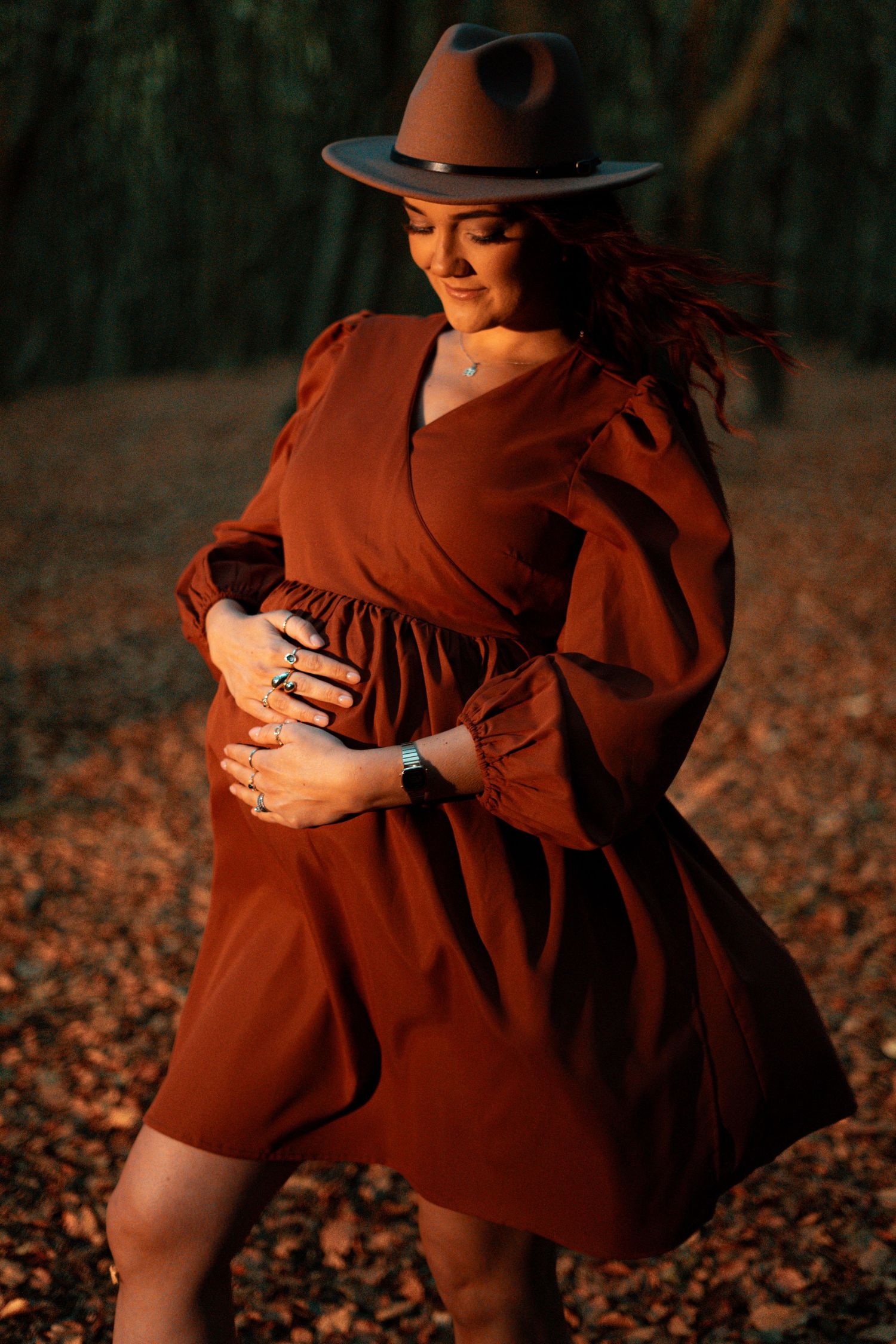 Close-up details of burgundy dress and hat against forest backdrop.