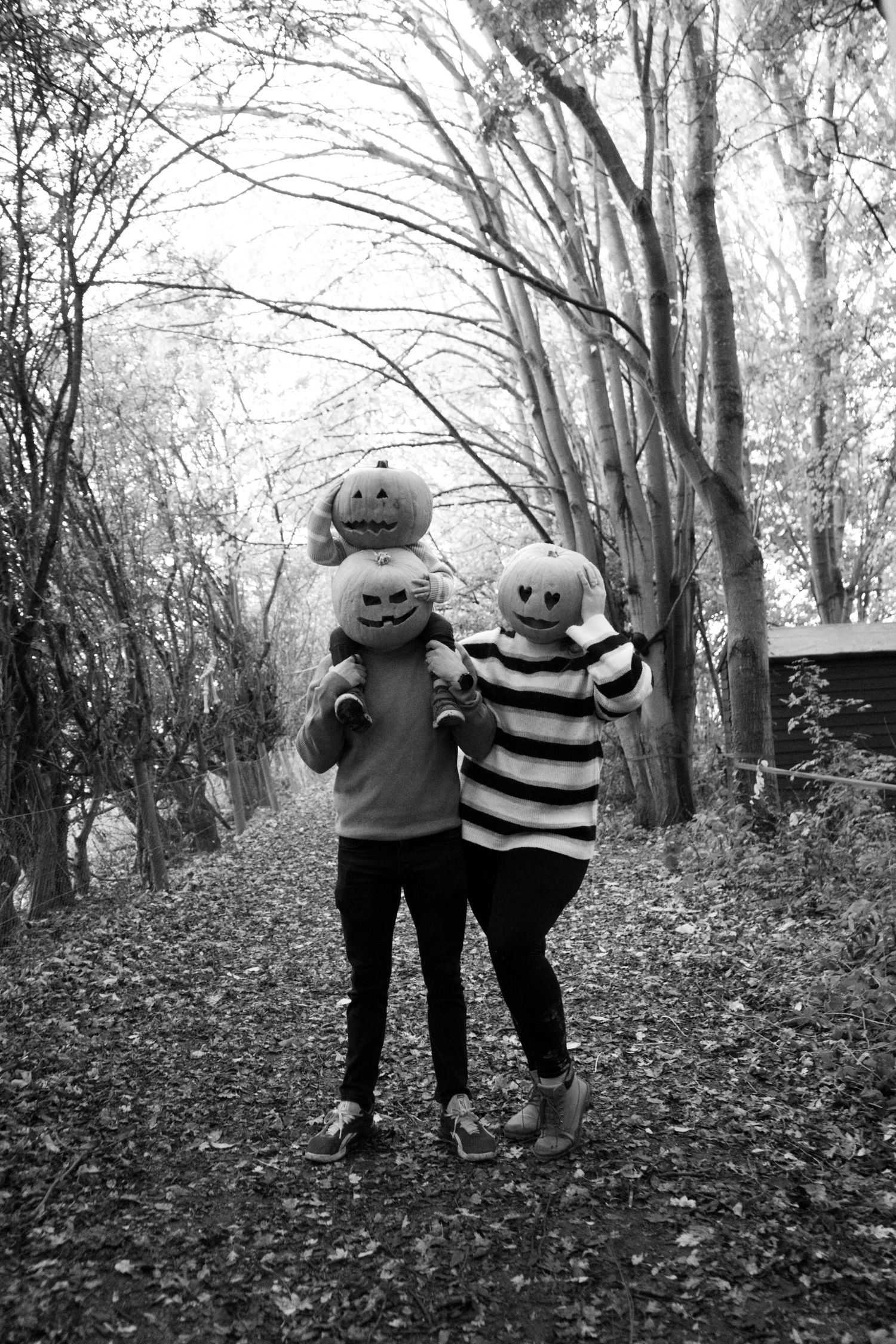 Black and white photo of two figures walking together on a leaf-strewn forest path.