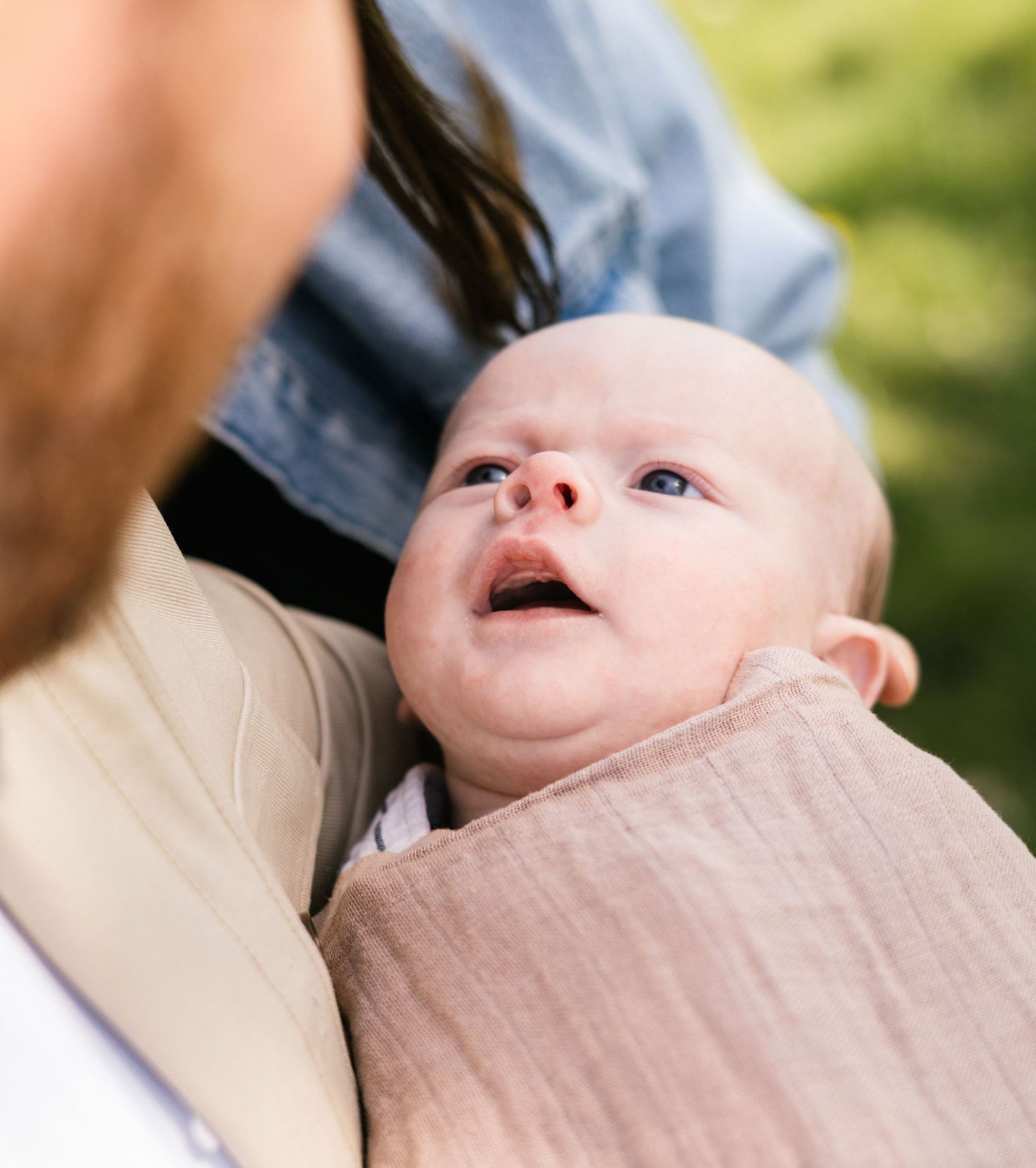 Baby wrapped in beige blanket enjoying outdoor family time.