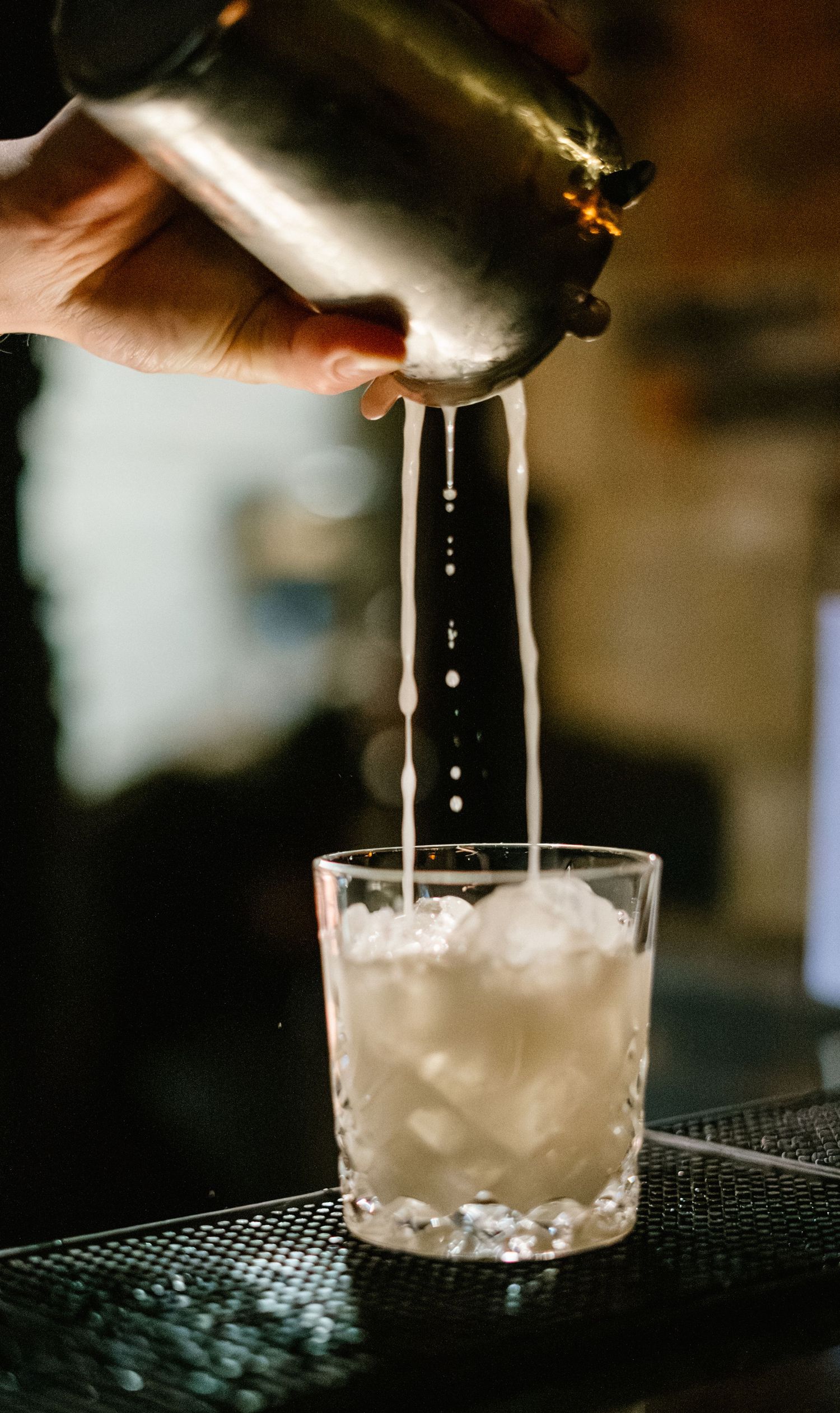 Straining a milky cocktail from a shaker into a crystal glass over ice.