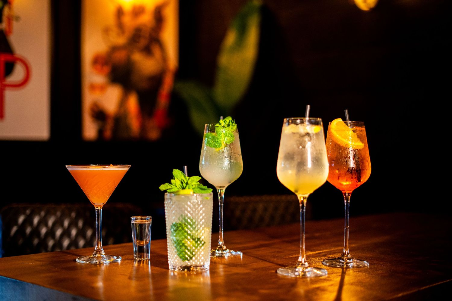 Artisanal cocktails arranged on dark wooden bar top with ambient lighting.