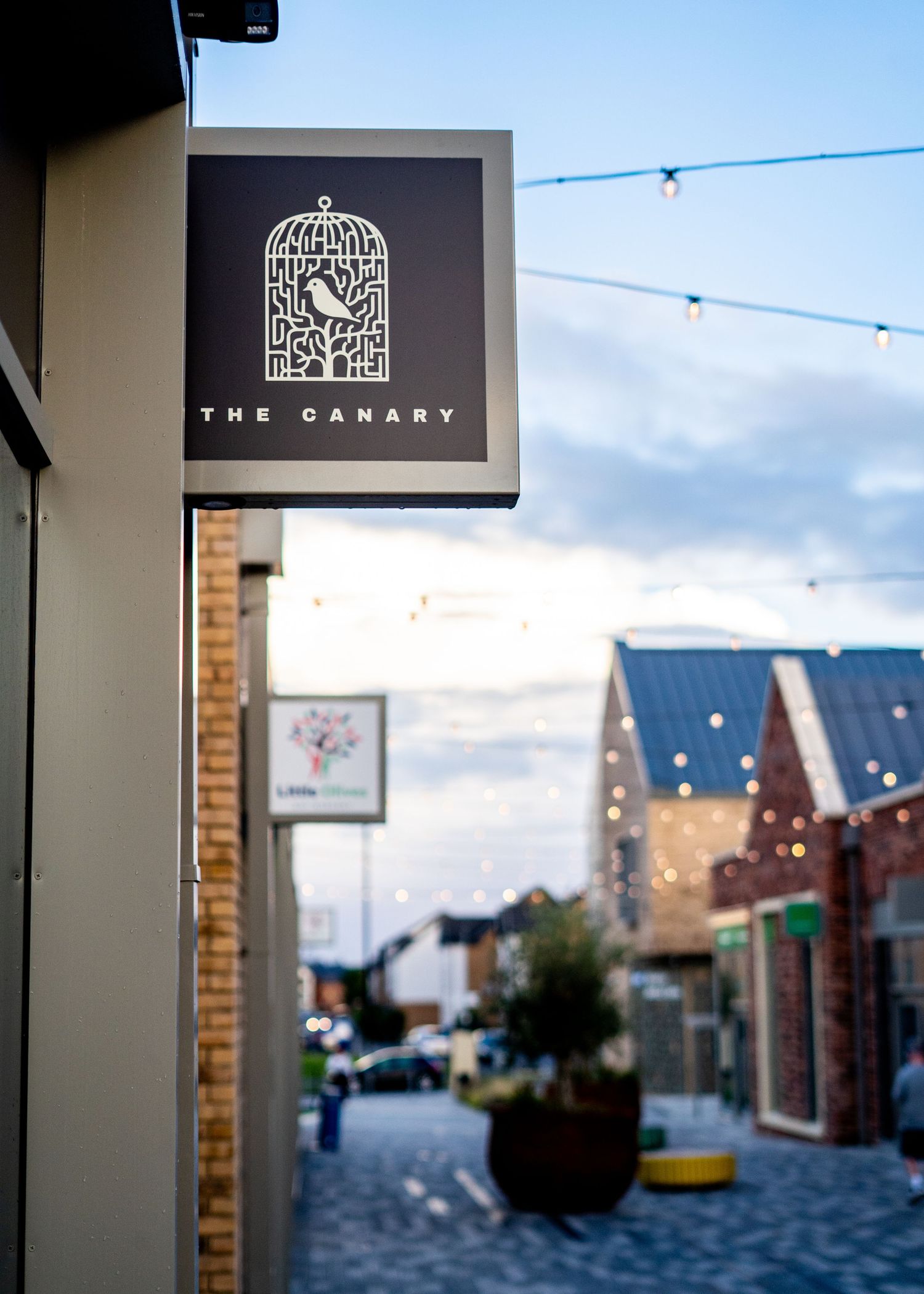 Black and gold sign for The Canary featuring a decorative birdcage logo design.