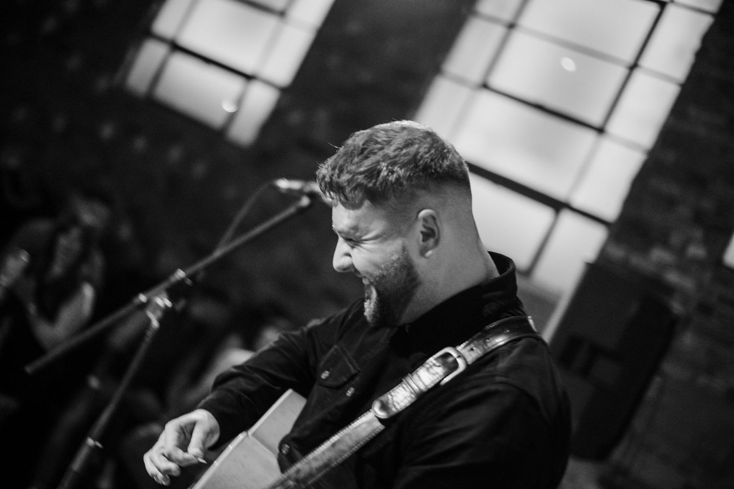 Black and white photo of a musician singing passionately while performing with a guitar.