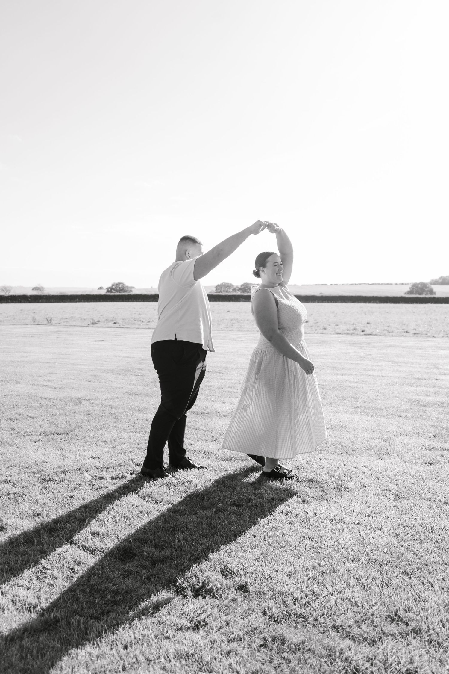 Couple sits together casting long shadows across a grassy field at sunset.