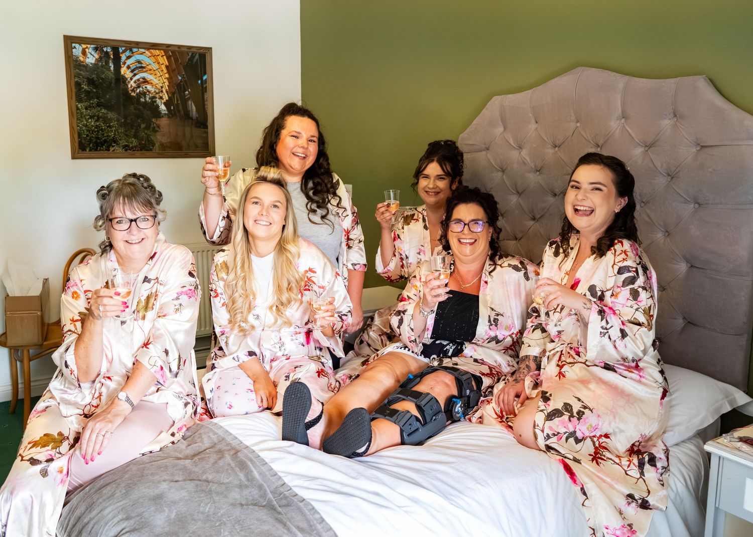 Wedding party members in floral robes pose together on bed during pre-ceremony preparations.
