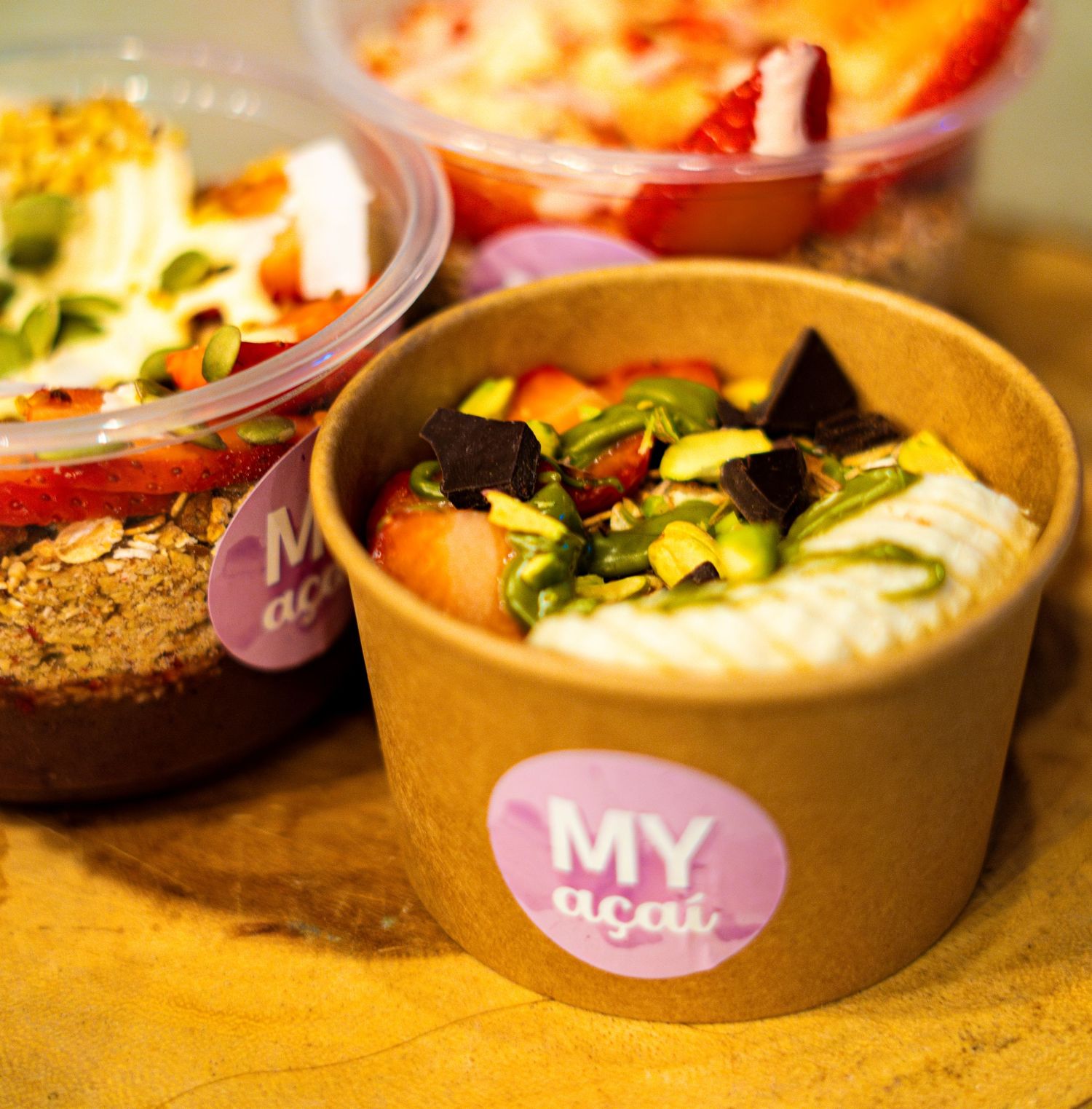 Artisanal food bowls with pink branding labels arranged on a wooden surface.