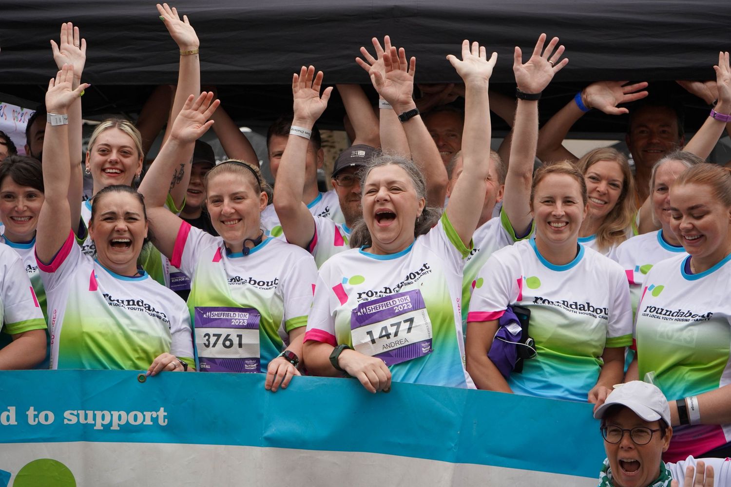 Enthusiastic runners raise their hands in celebration at an outdoor charity event.
