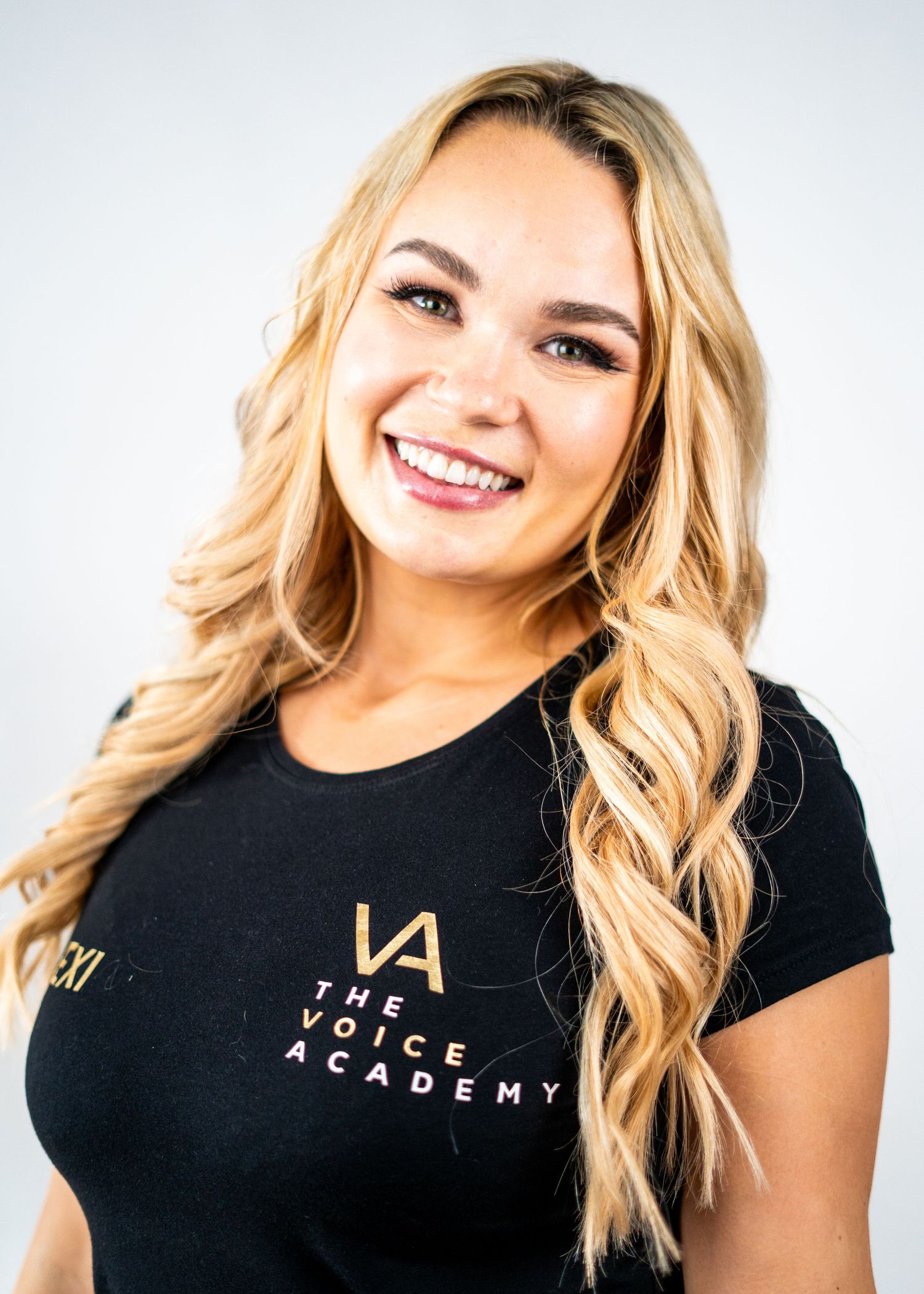 Person wearing a black Voice Academy t-shirt with blonde wavy hair and bright smile.