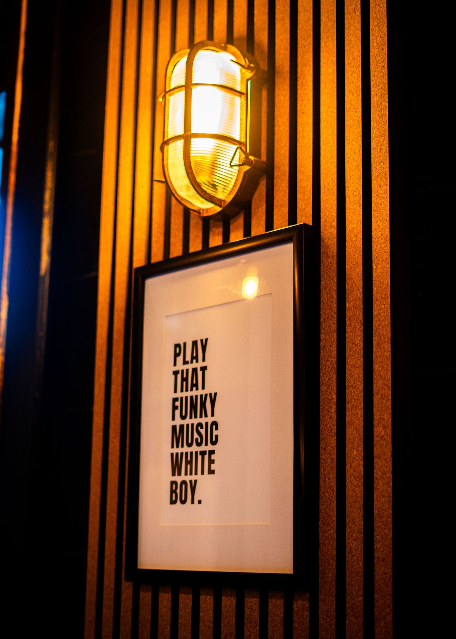 Black wall with white text posters reading 'Play That Funky Music' illuminated by industrial lights.