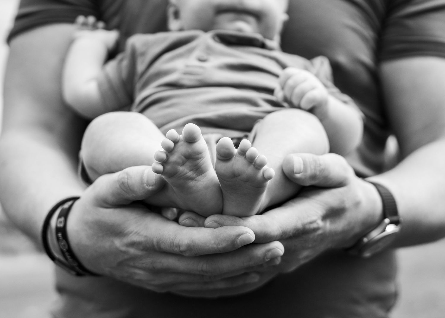 Close-up black and white photo of tiny baby feet being gently held in adult hands.