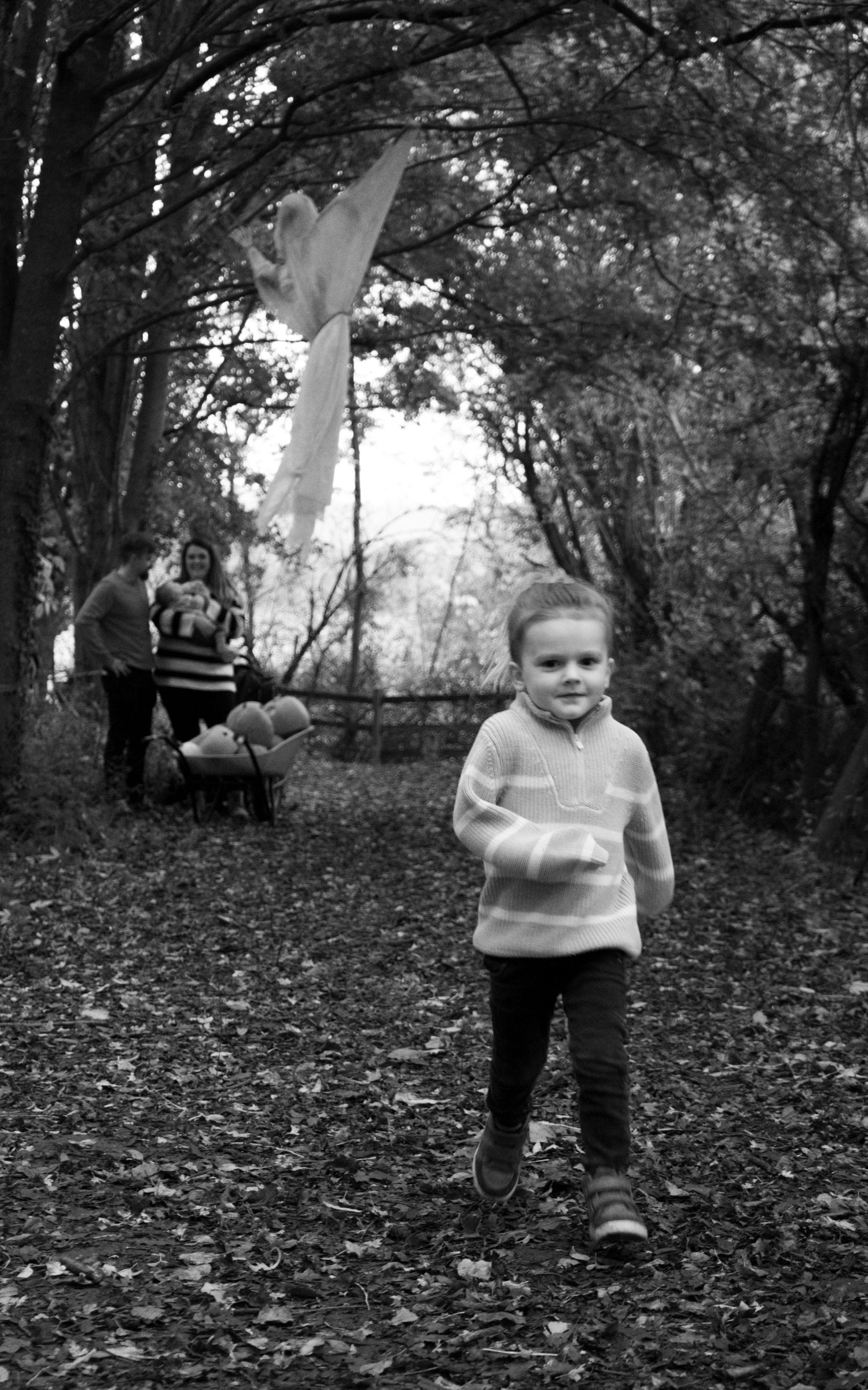 A playful moment captured in black and white on a wooded trail covered in autumn leaves.