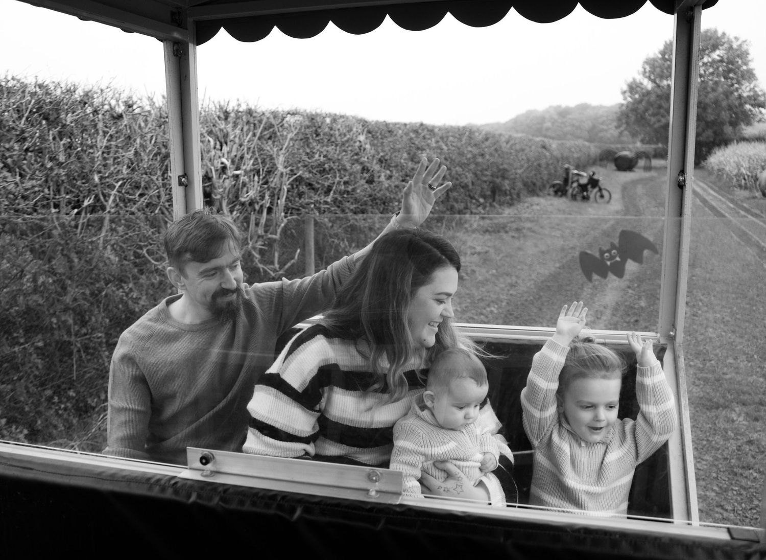 Black and white photo of people sitting under a covered wagon frame.