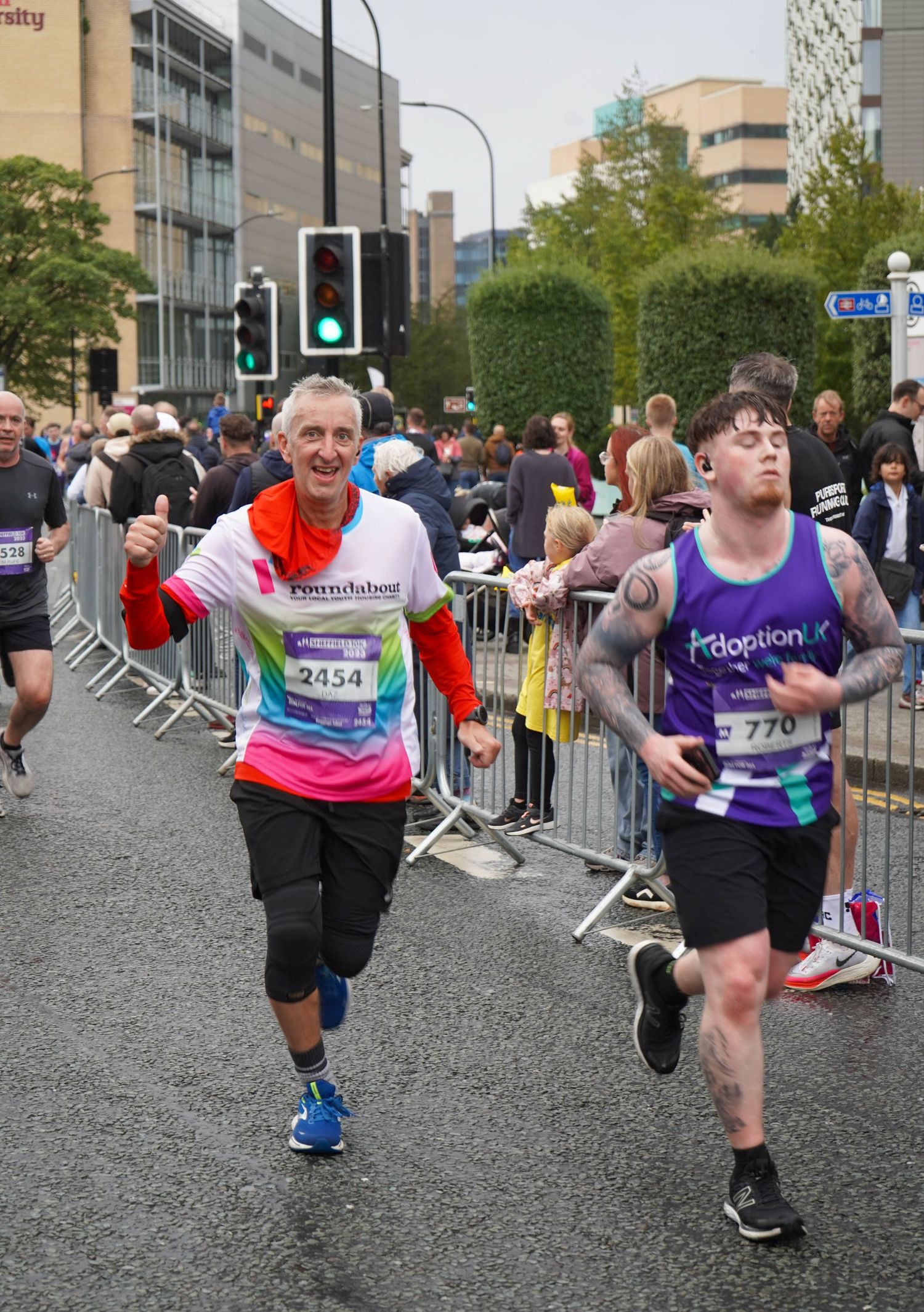 Participants in numbered bibs running along a barricaded street during a community race.