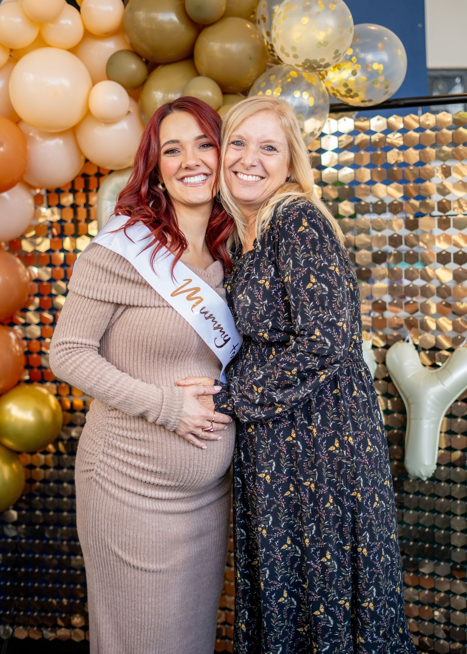 Friends pose together at celebration with gold and peach balloon backdrop and metallic wall decor.