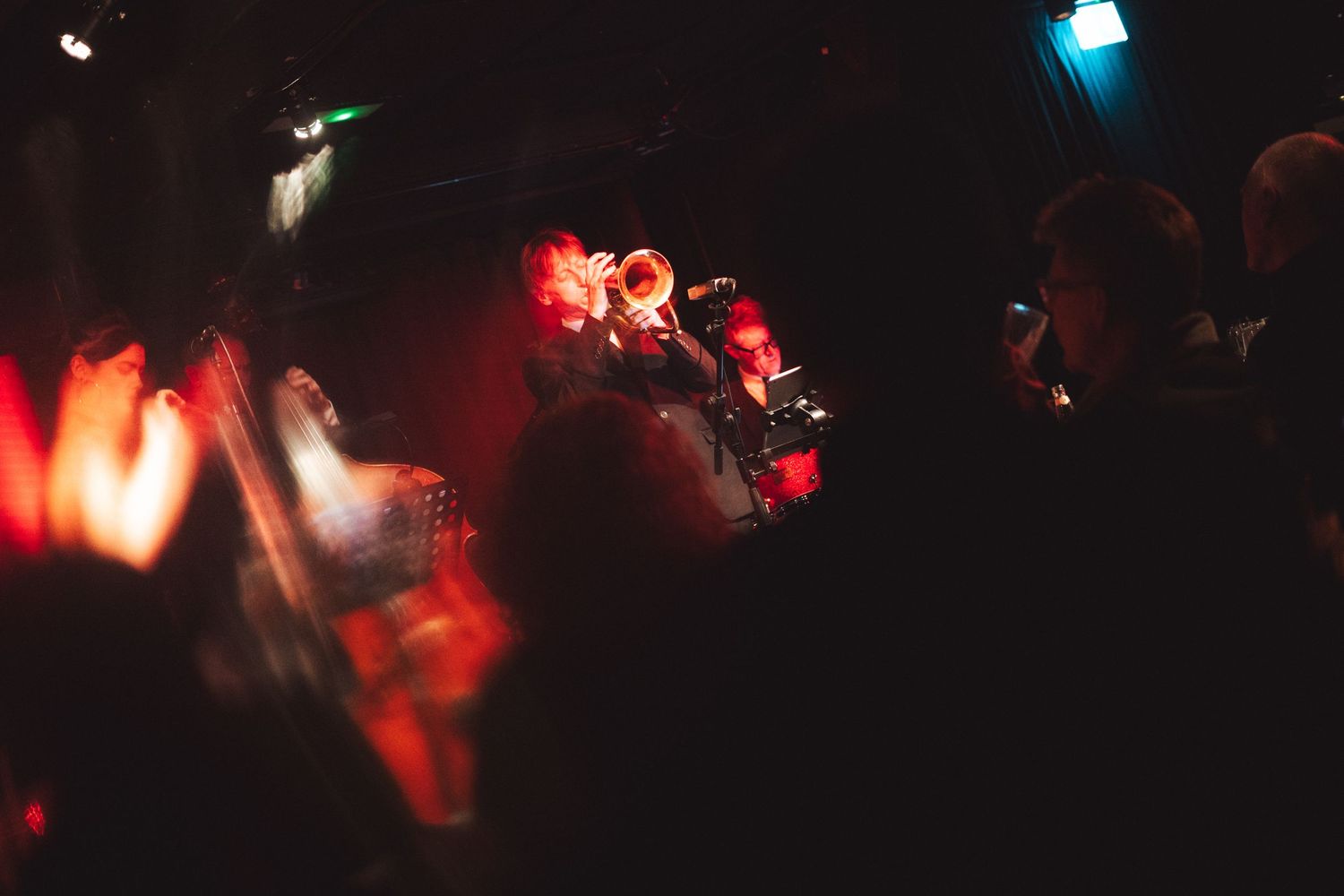 A concert scene with red stage lighting and silhouetted figures in the darkness.