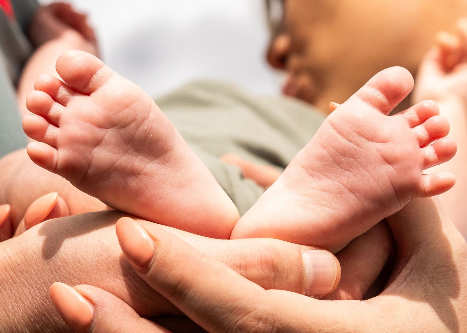 Close-up of tiny newborn baby feet being gently held by caring hands.