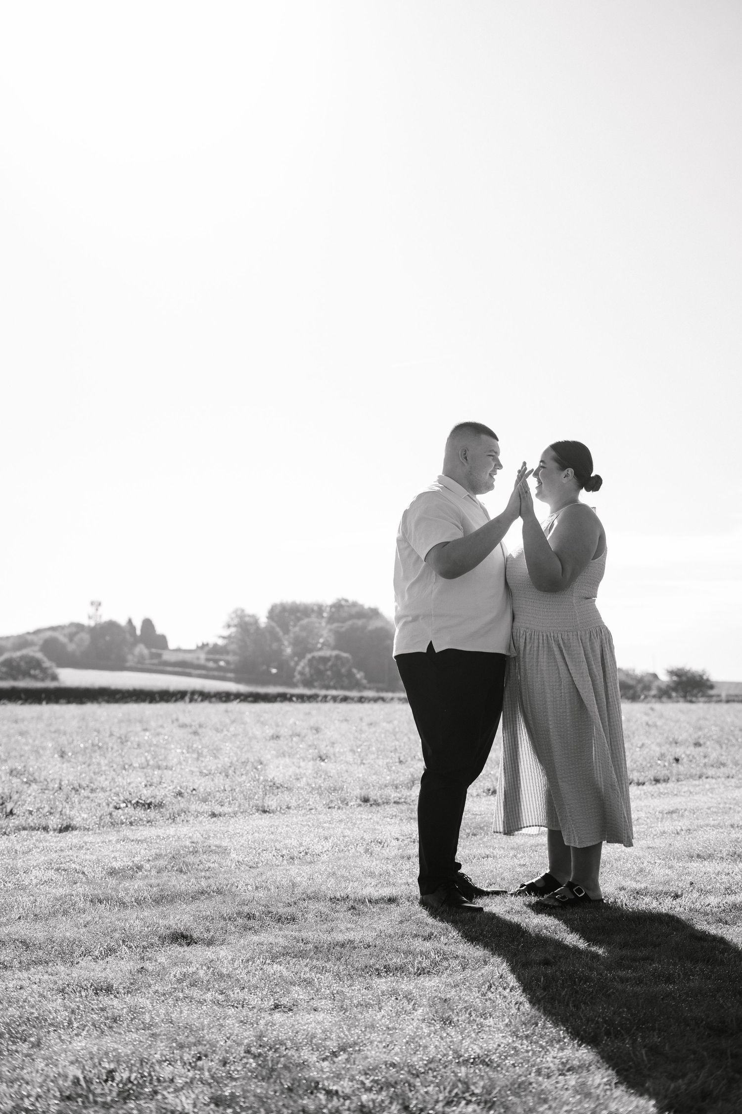 Black and white portrait of couple creating dramatic shadows on grassy field.