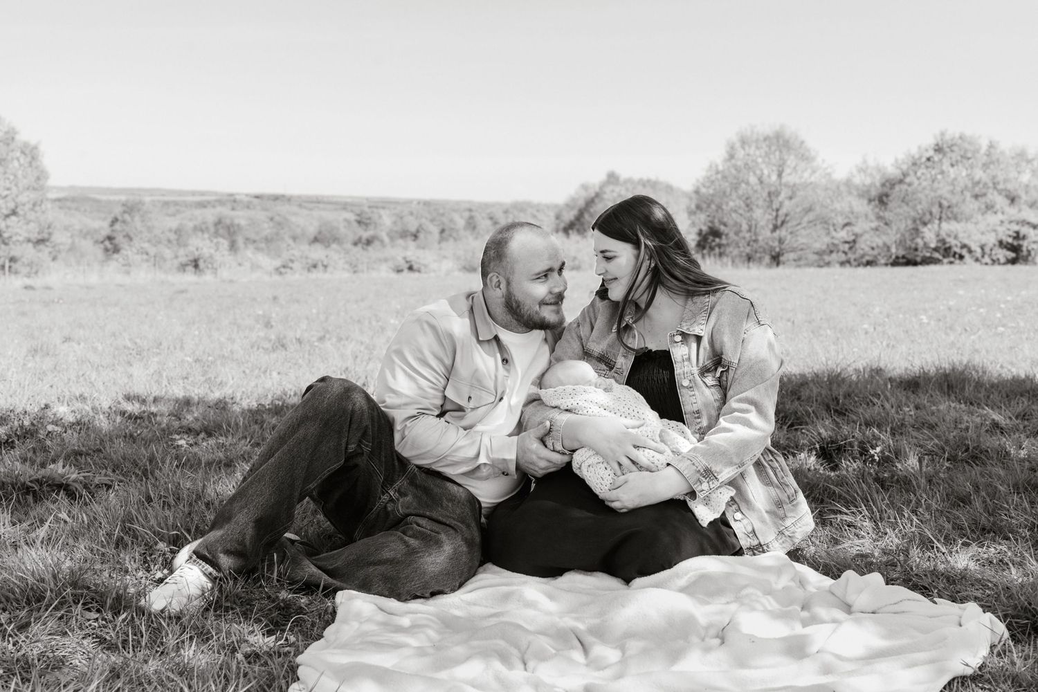 A tender outdoor family moment on a blanket in a grassy field on a sunny day.