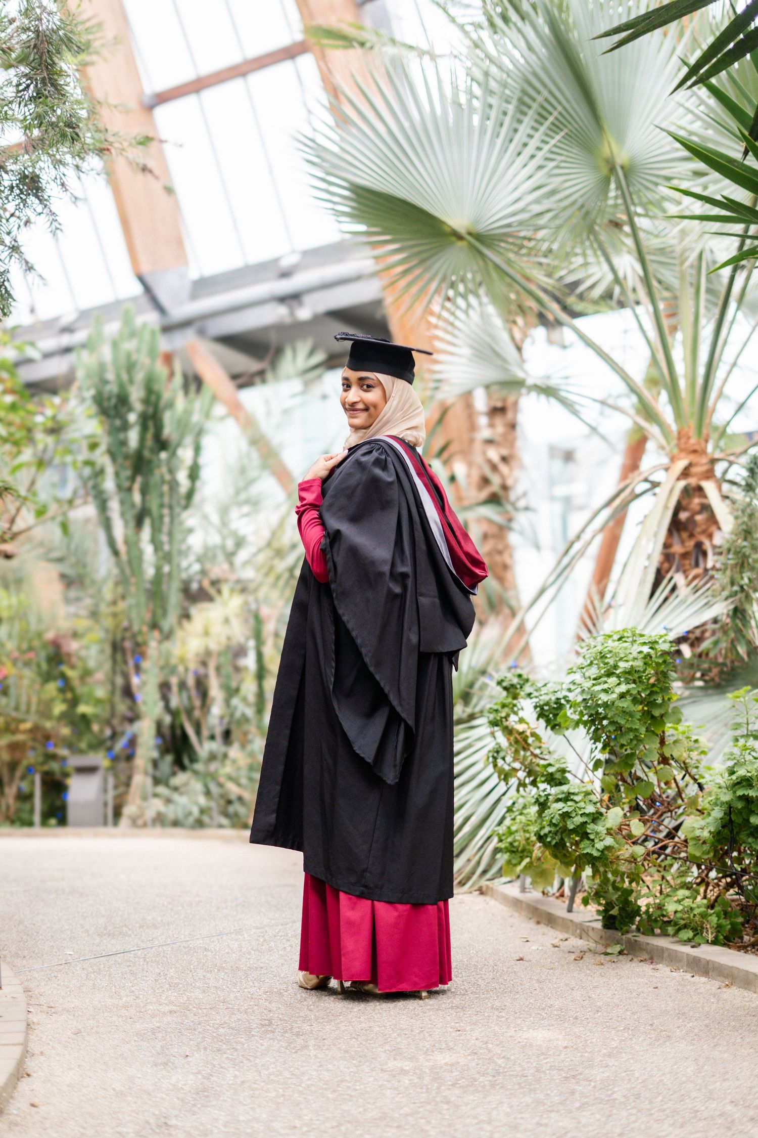 Graduation photoshoot in a greenhouse with palm trees and natural lighting.