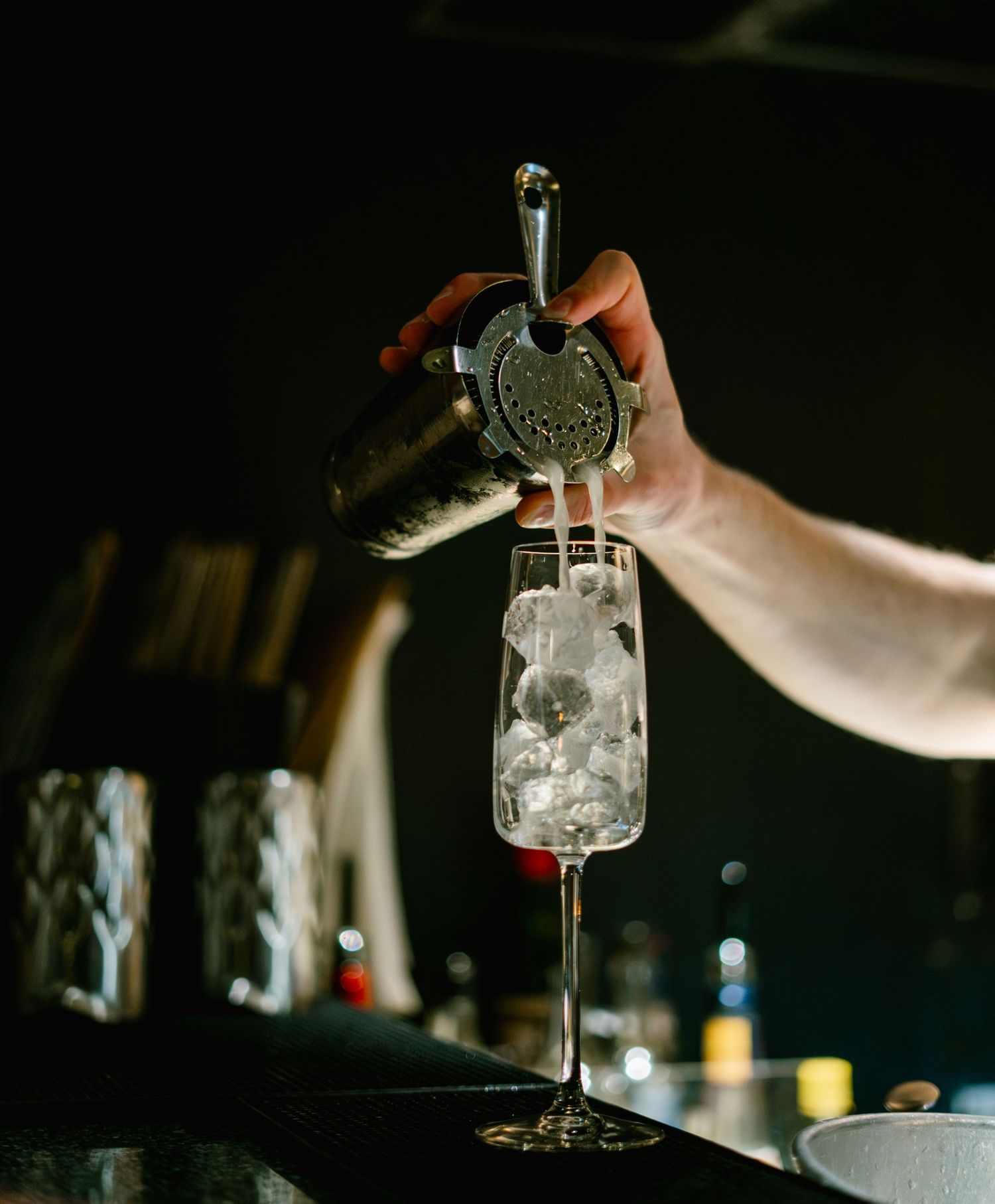 Hand adding ice to a cocktail glass using professional bar tools.