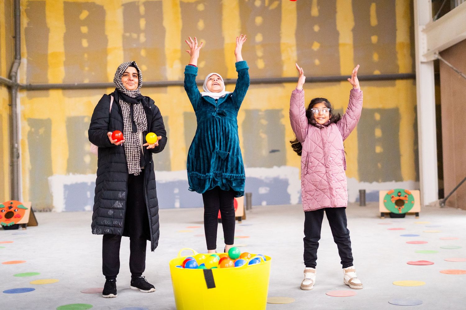 Three people with raised arms participating in an indoor activity with yellow walls and colorful floor.