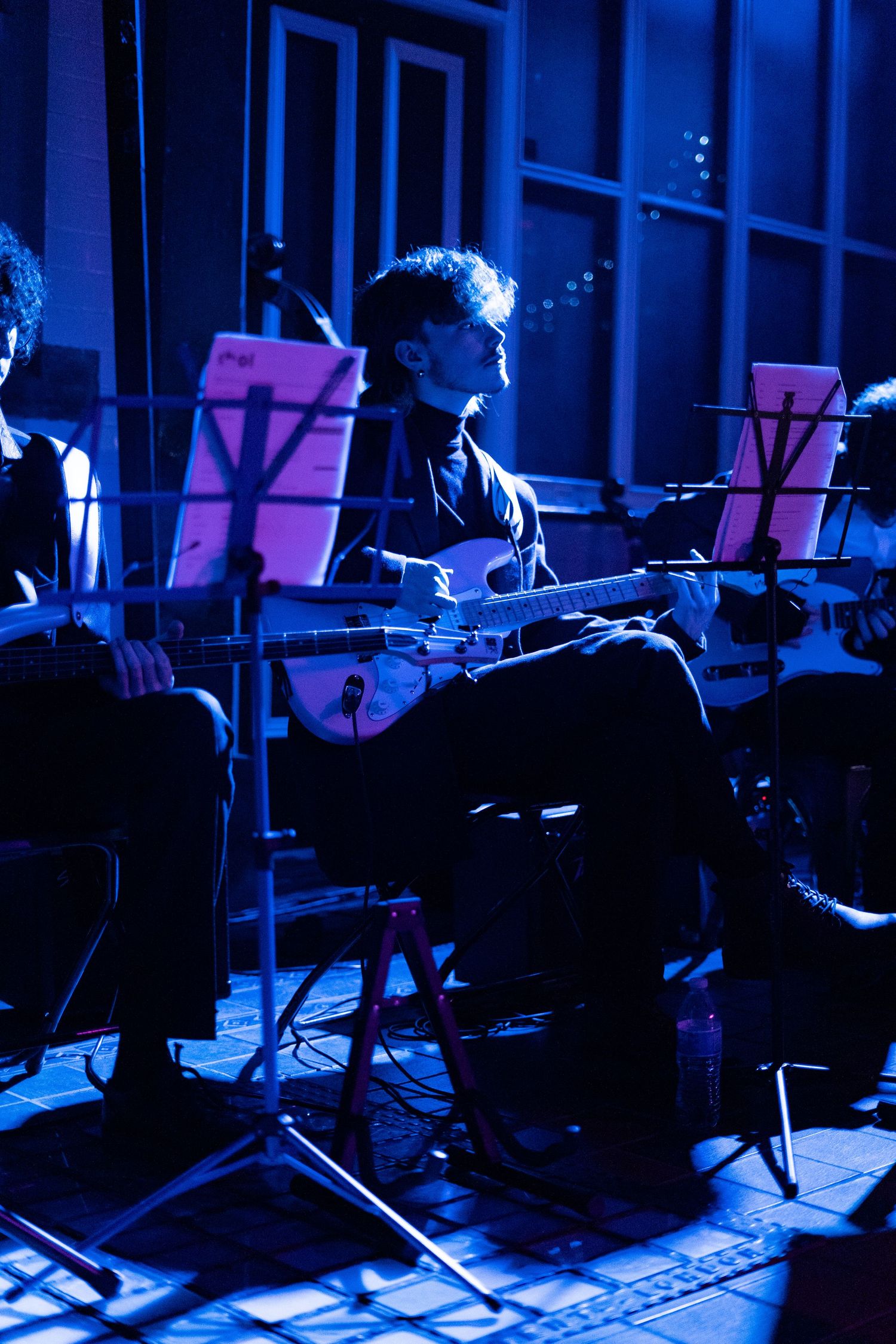 Musicians performing on stage in dramatic blue lighting at night.