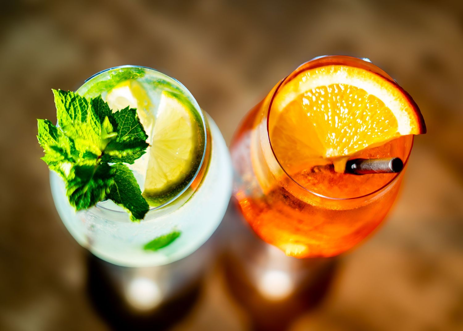 Row of colorful cocktails garnished with citrus and herbs on bar counter.